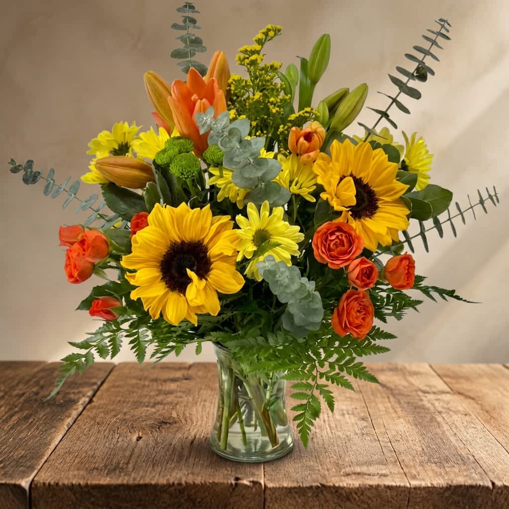 Thankful for You (BB) - Celebrate the spirit of gratitude and appreciation with our "Thankful for You" floral arrangement. Expertly curated with a mix of vibrant orange lilies, sunflowers, orange spray roses, green button poms.This arrangement is perfect for Thanksgiving, autumn, and fall.