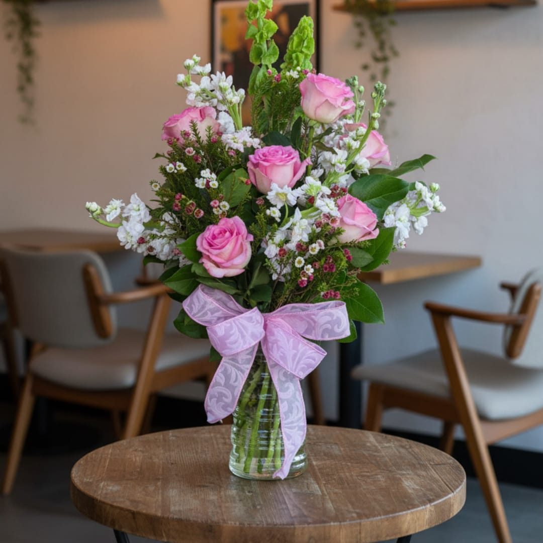 Pink roses and white filler flowers in a glass vase with a pink ribbon