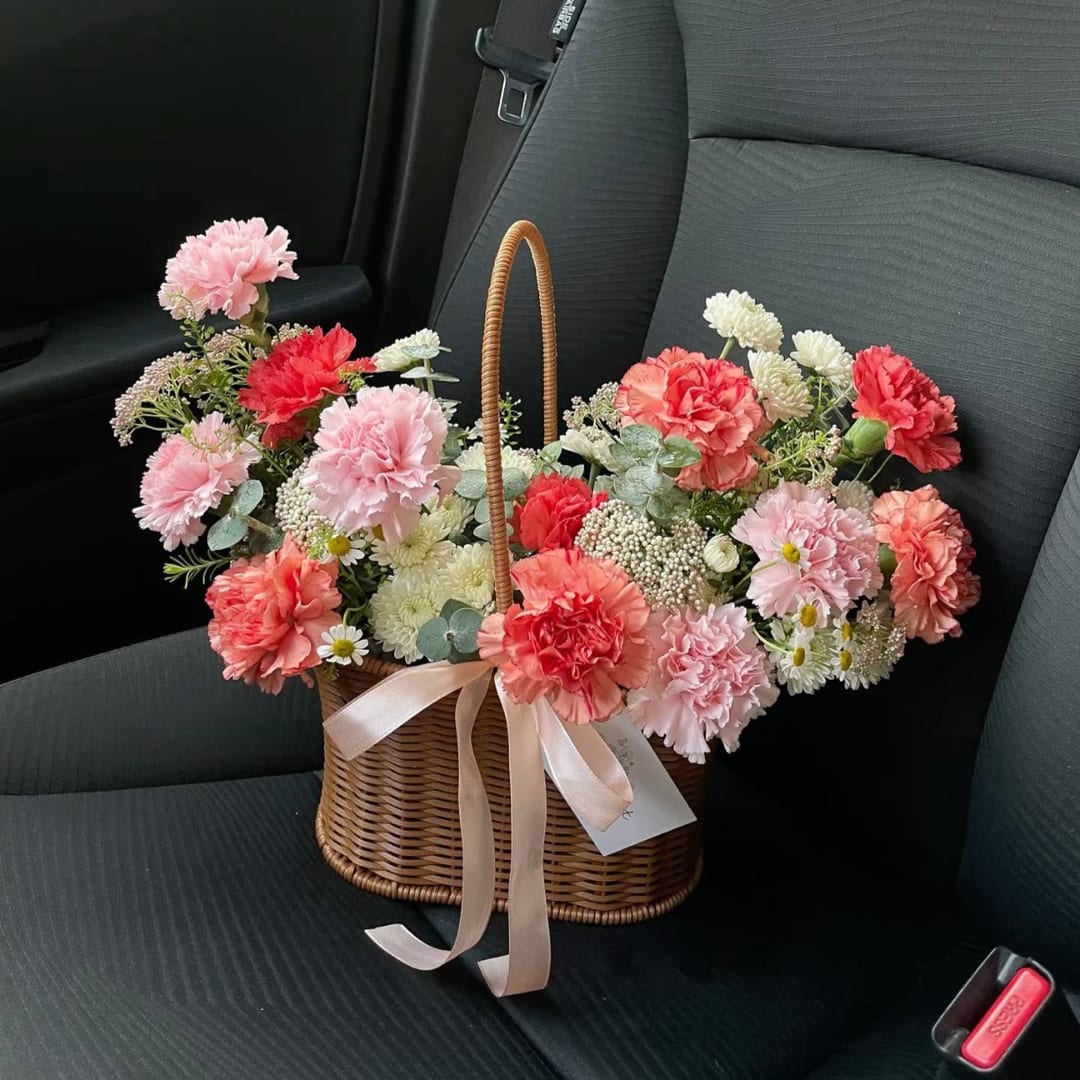 Basket of pink and coral carnations with white daisies on a car seat