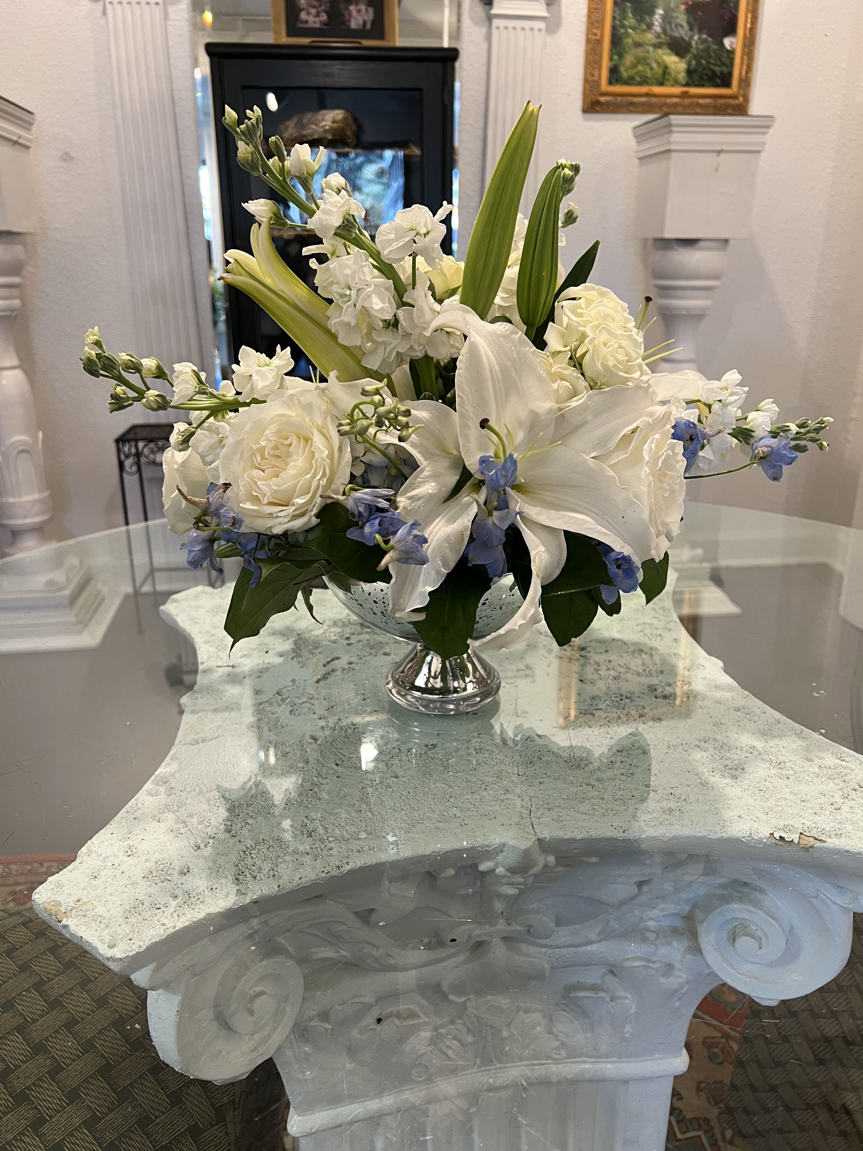 Low white and blue flower arrangement with lilies and roses in a silver pedestal vase