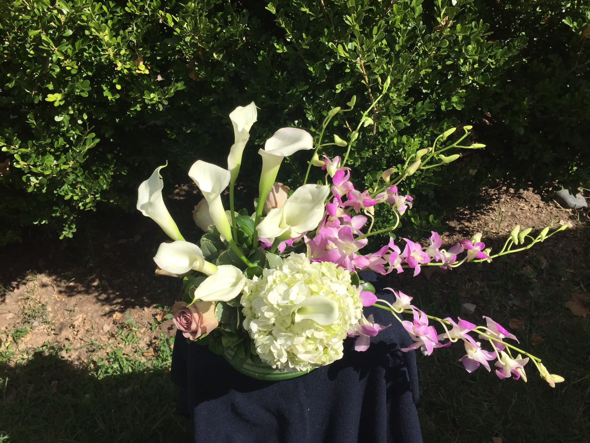 White calla lilies and pink orchids in a low vase with a pale hydrangea bloom