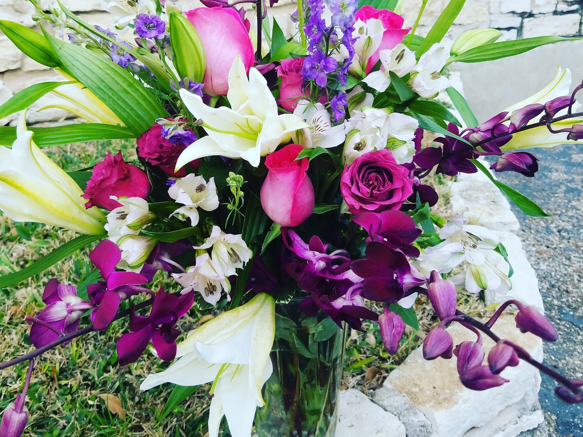 Bouquet of pink roses, white lilies, and purple orchids in a glass vase