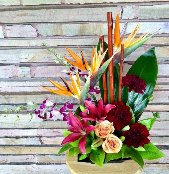 Tropical bouquet with bird of paradise, orchids, roses, and dark red blooms in a vase