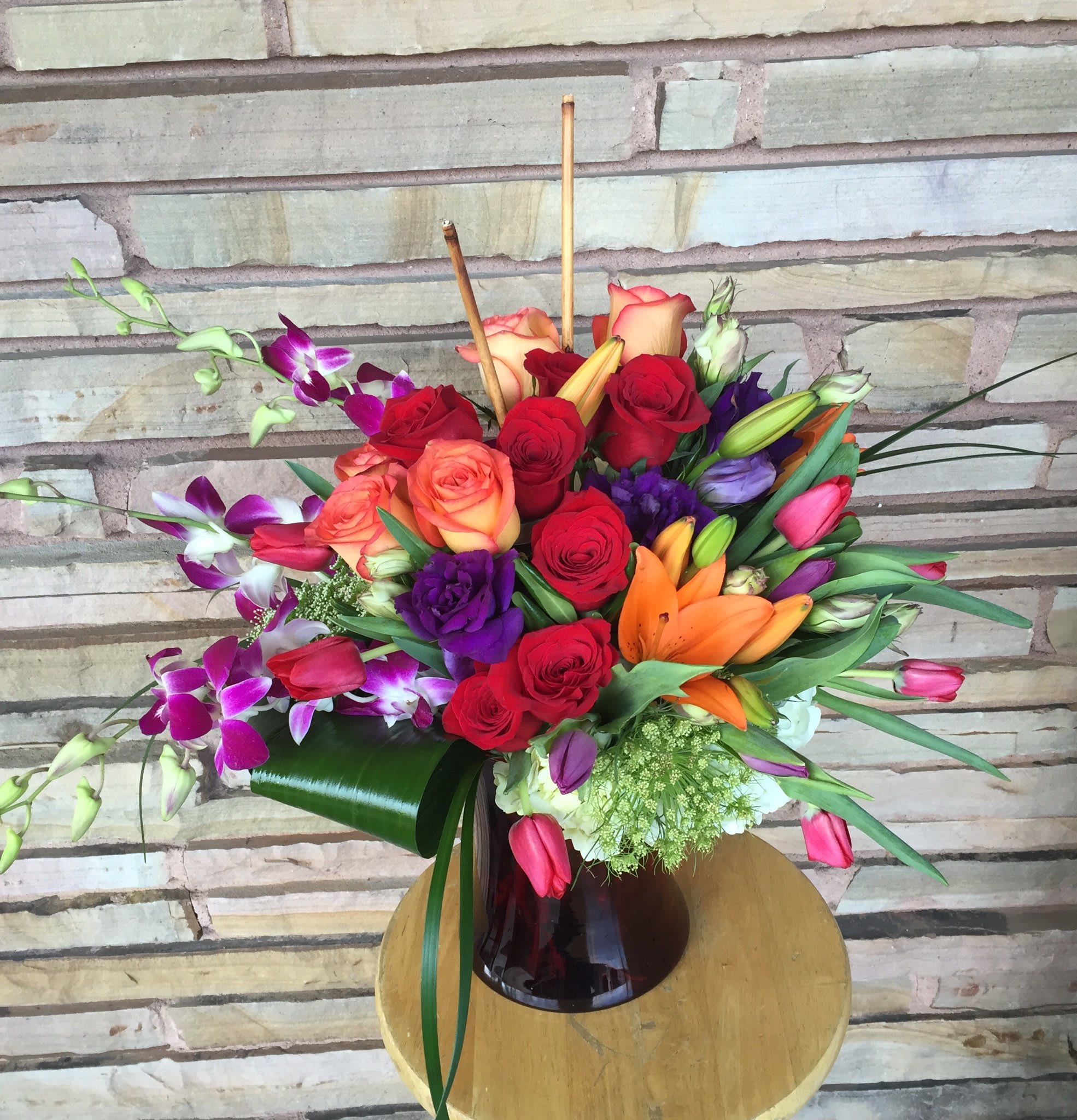 Mixed bouquet of roses, lilies, and orchids in a dark glass vase