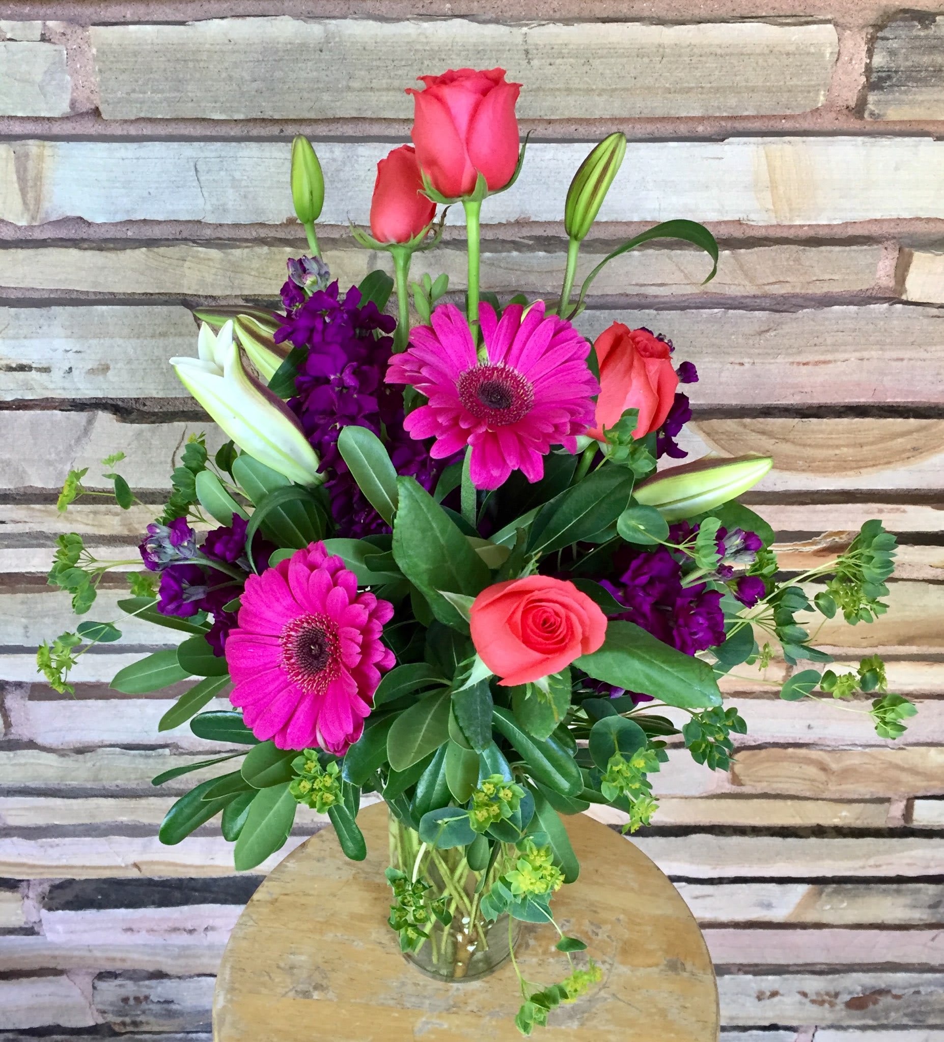 Pink roses and gerbera daisies in a glass vase with purple flowers