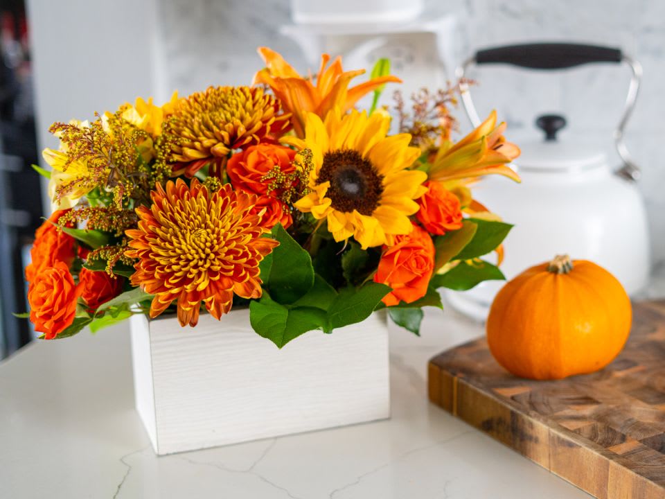 Orange and yellow autumn bouquet in a white box beside a small pumpkin