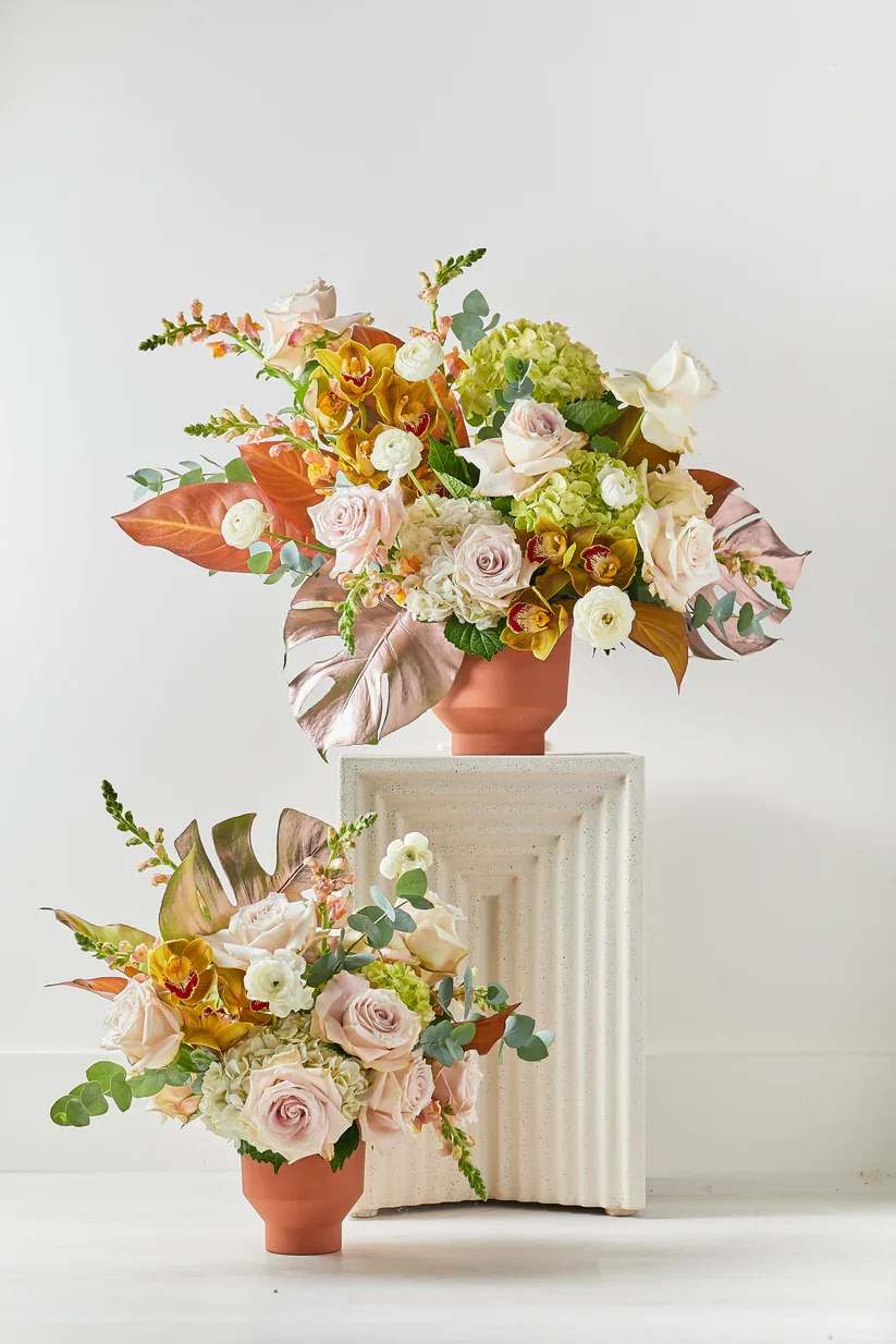 Two pastel floral arrangements in terracotta vases on pedestals