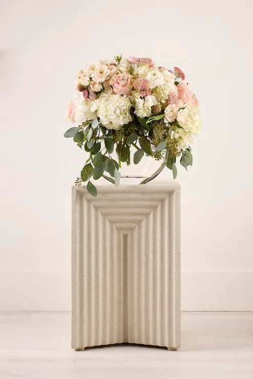 Blush and white floral arrangement on a pedestal with trailing greenery
