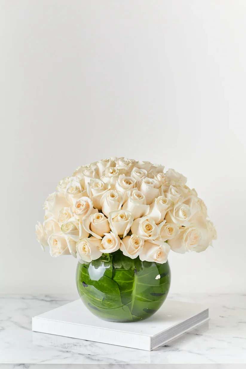 Cream roses arranged in a round green glass vase