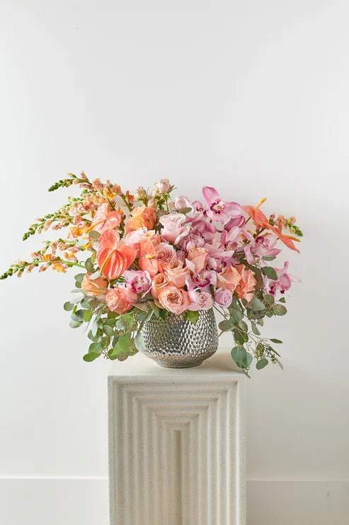 Pink and peach floral arrangement in a textured silver vase