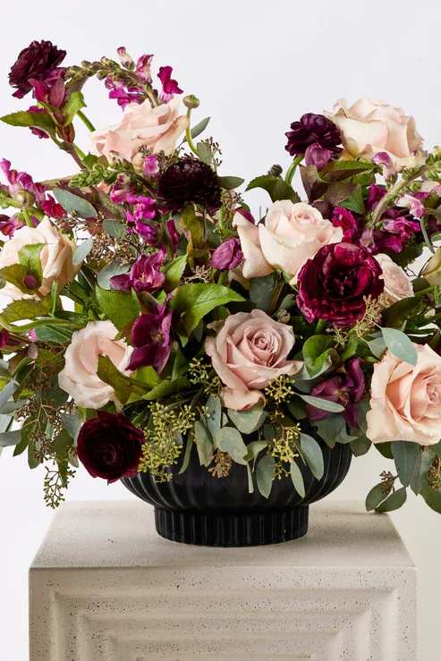 Bouquet of pale pink roses and deep burgundy flowers in a black vase