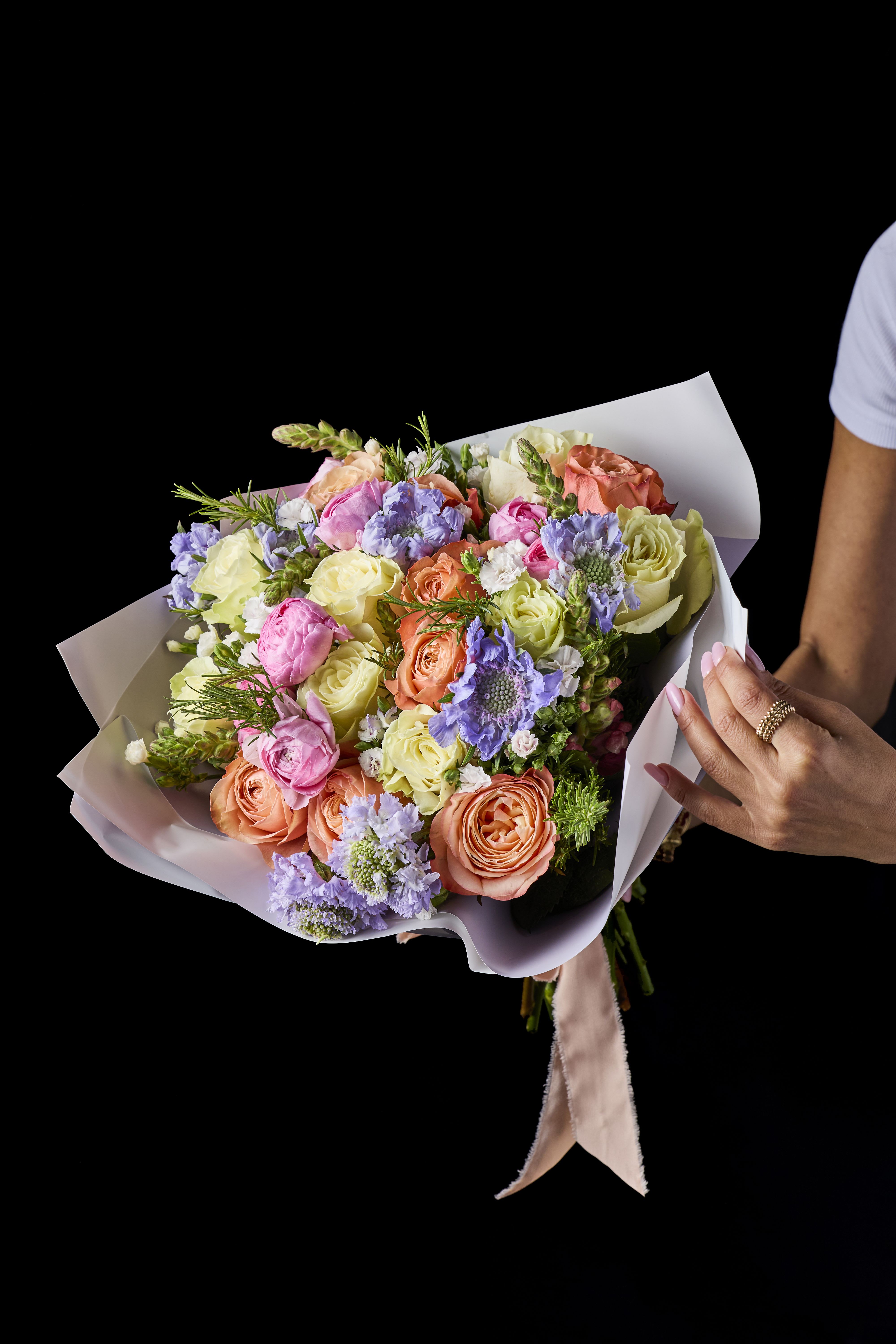 Hand-tied bouquet of pastel roses and purple blooms in white wrap