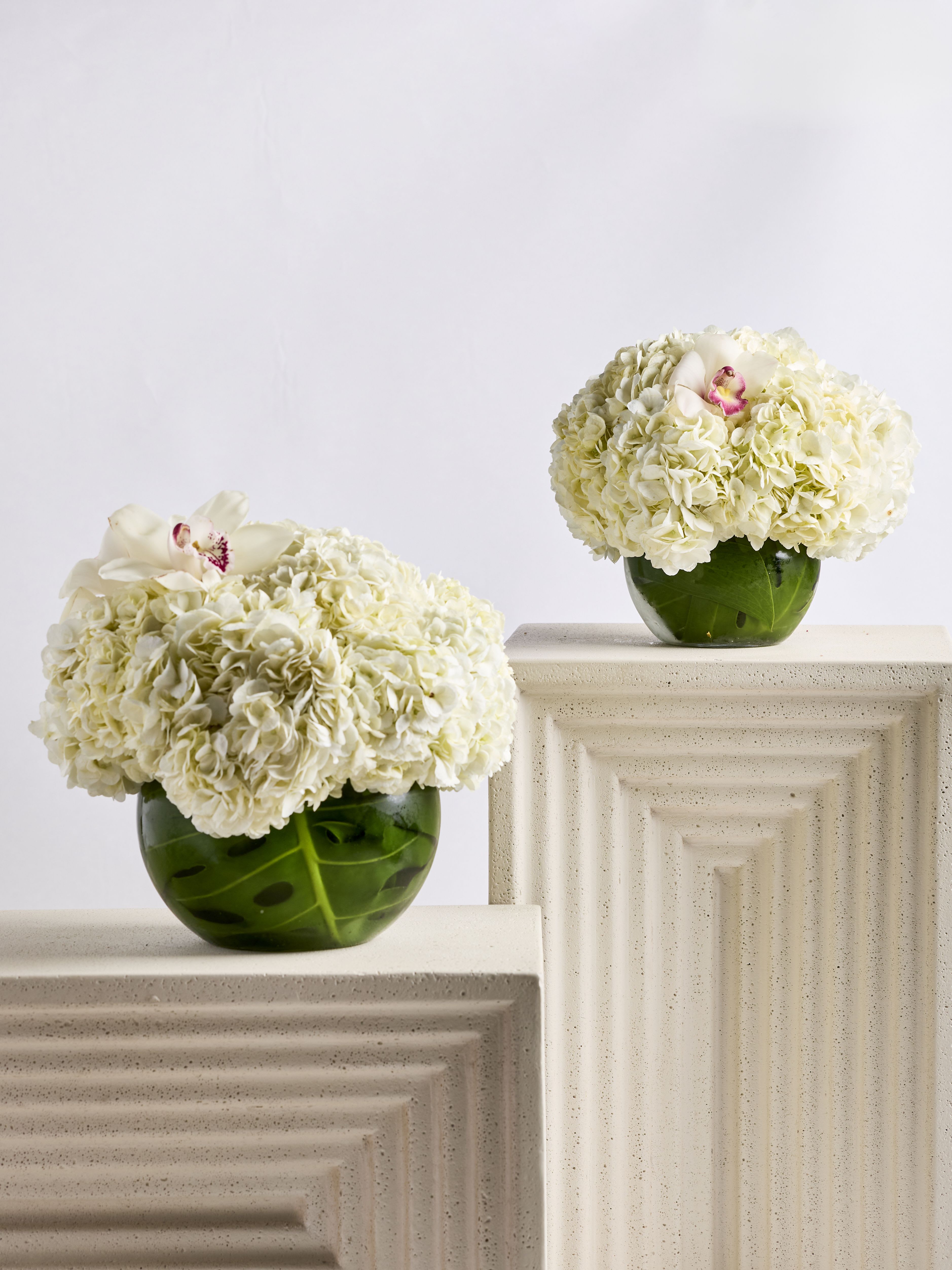 Two white hydrangea arrangements in green glass vases on pedestals