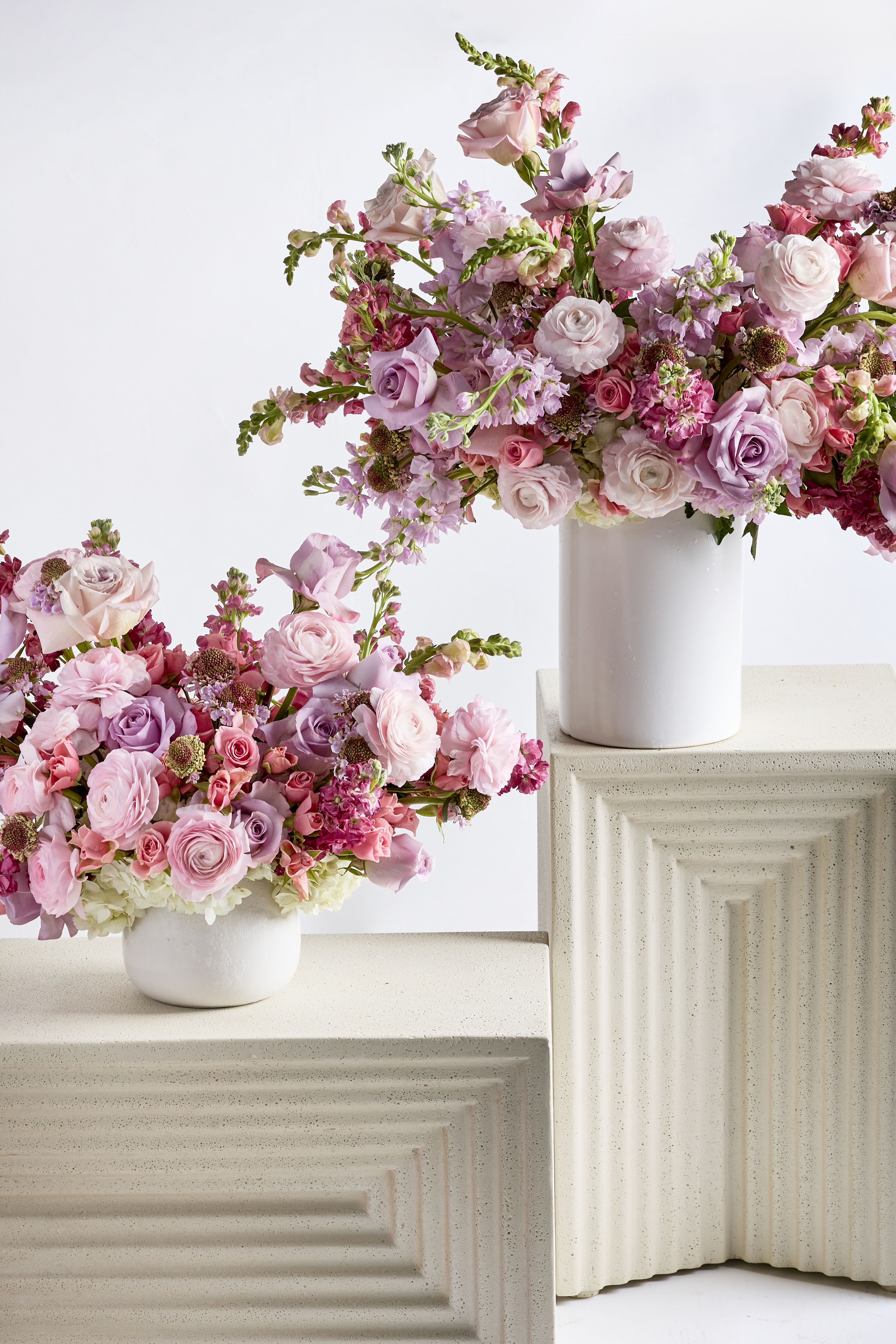 Two pink floral arrangements in white vases on textured pedestals
