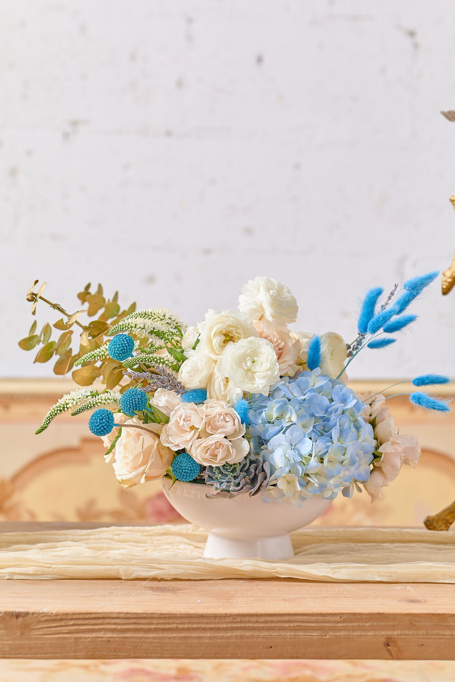 Pastel floral arrangement in a white pedestal bowl with blue accents