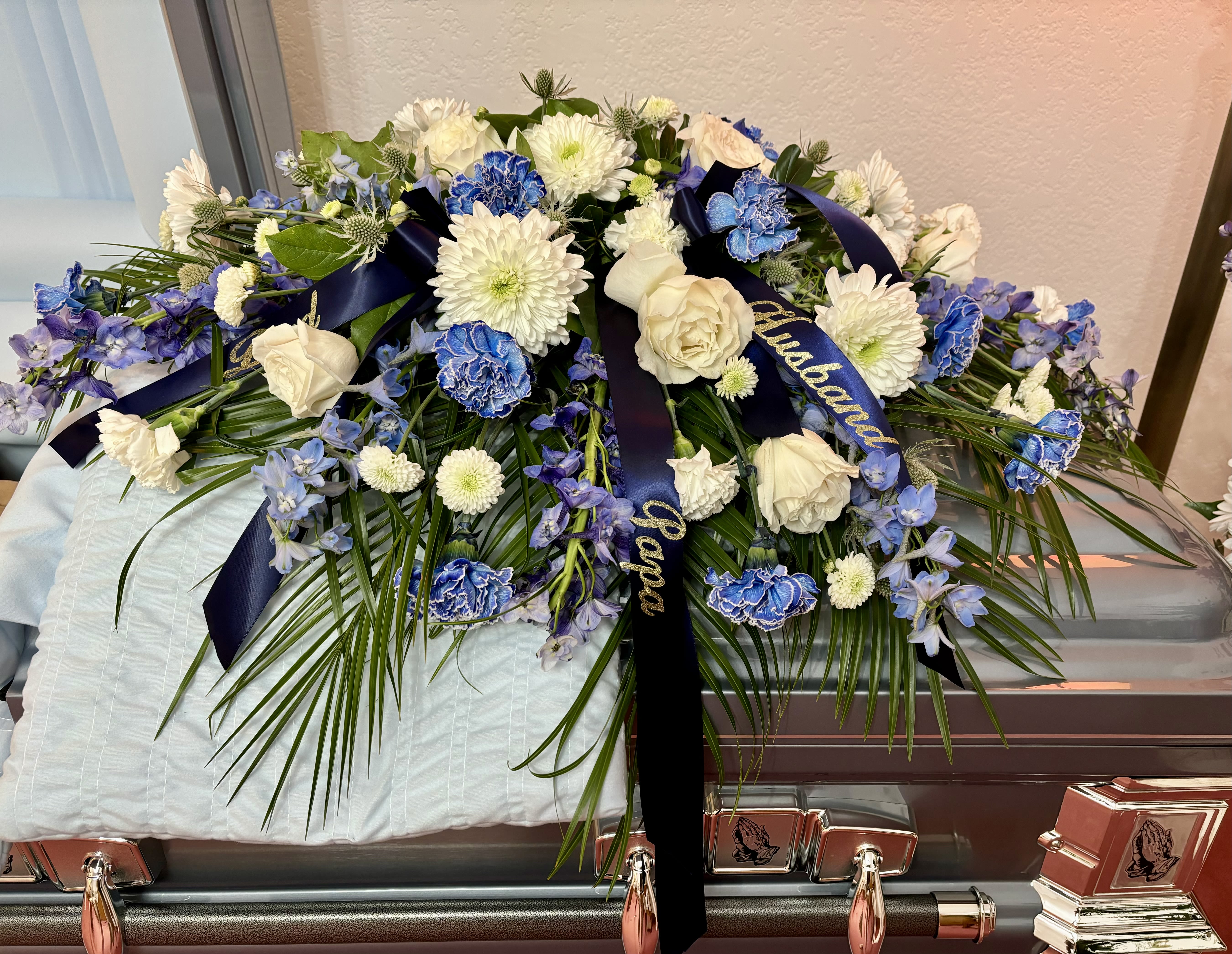 White and blue floral casket spray with ribbon on a coffin