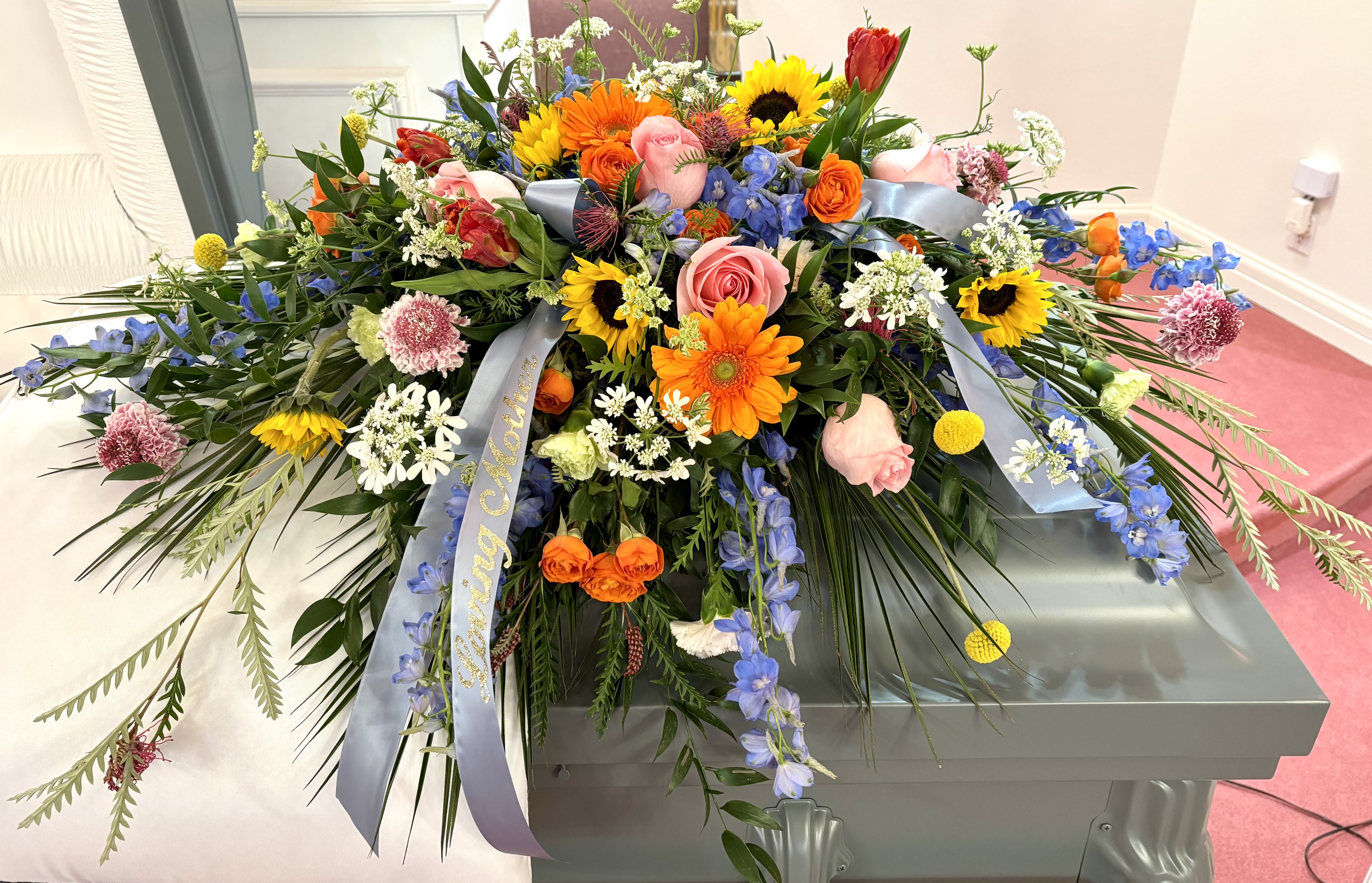Large casket spray with mixed colorful flowers and blue ribbons