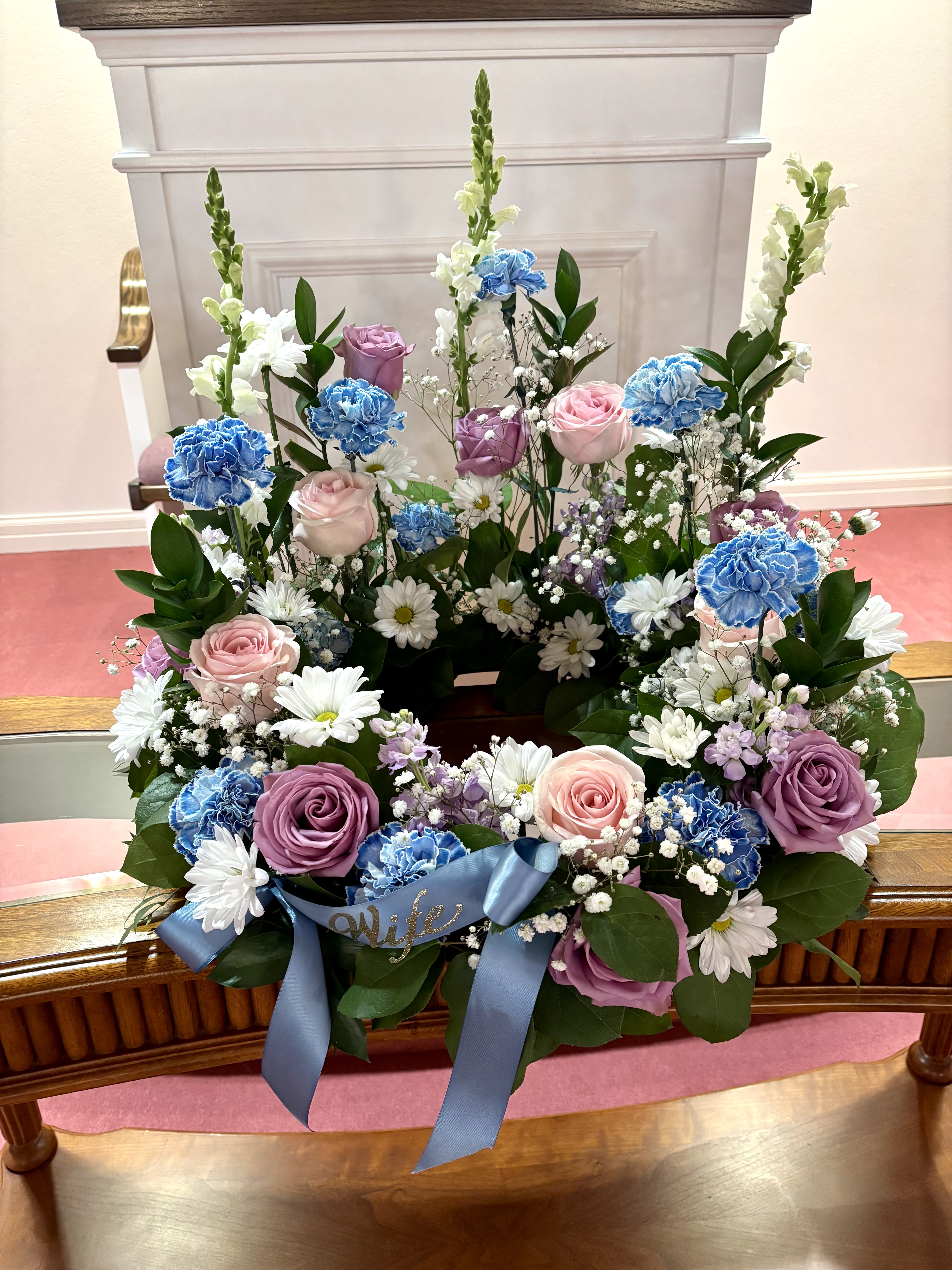 Floral wreath with pink and purple roses, blue carnations, and white daisies