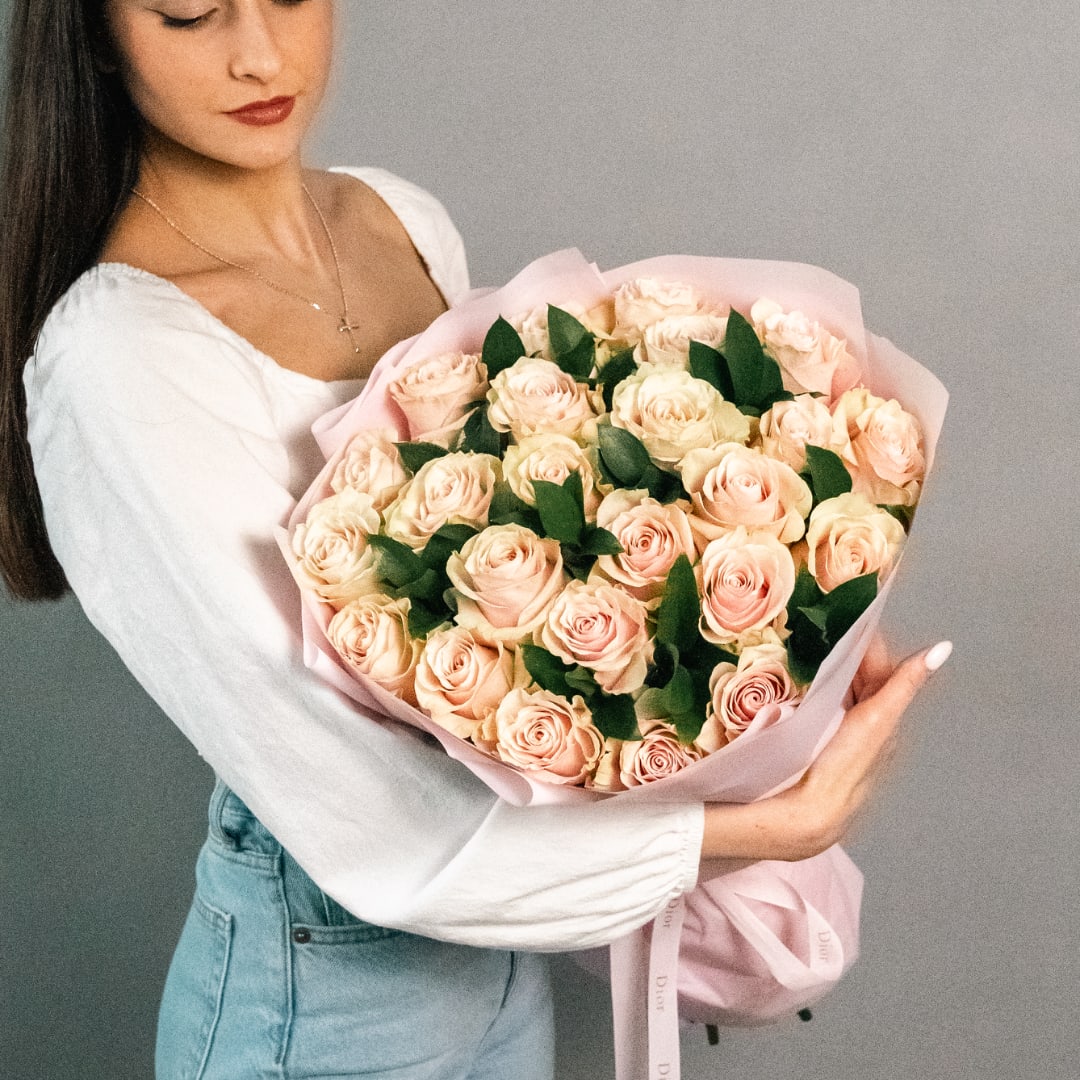 Woman holding a large bouquet of pale pink roses wrapped in pink paper