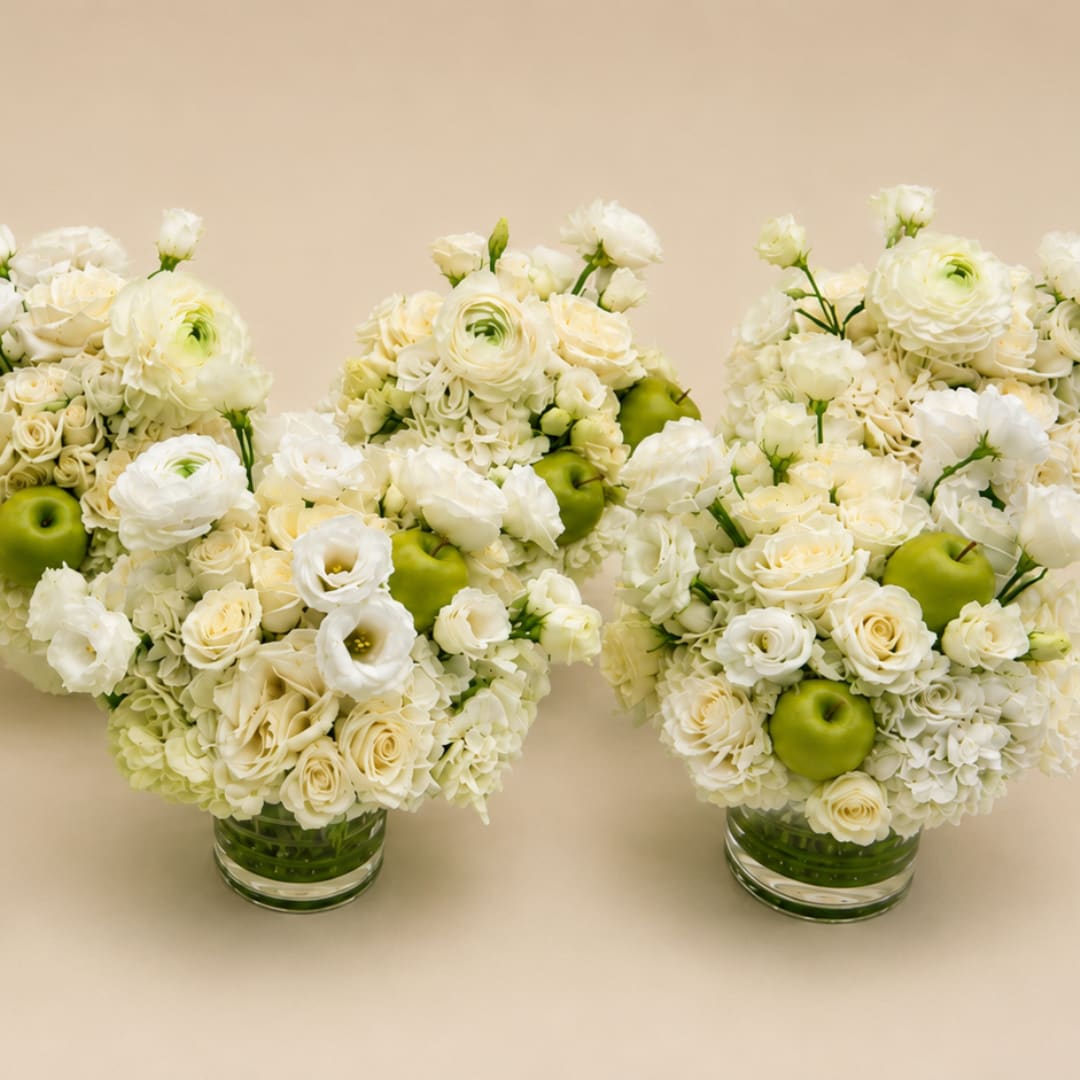 Three white floral arrangements with green apples in clear glass vases