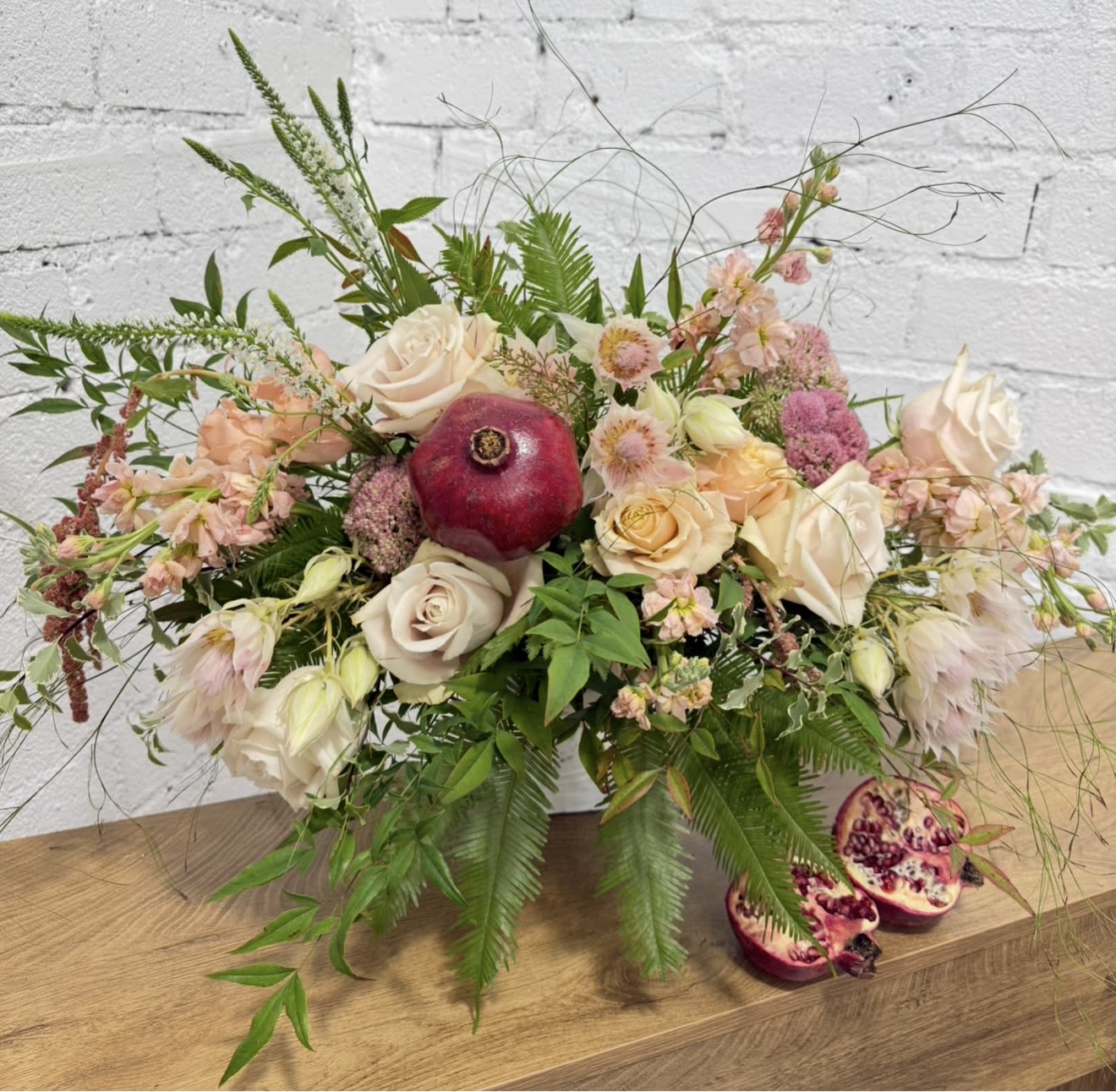 Low floral arrangement with cream and blush roses and a pomegranate centerpiece