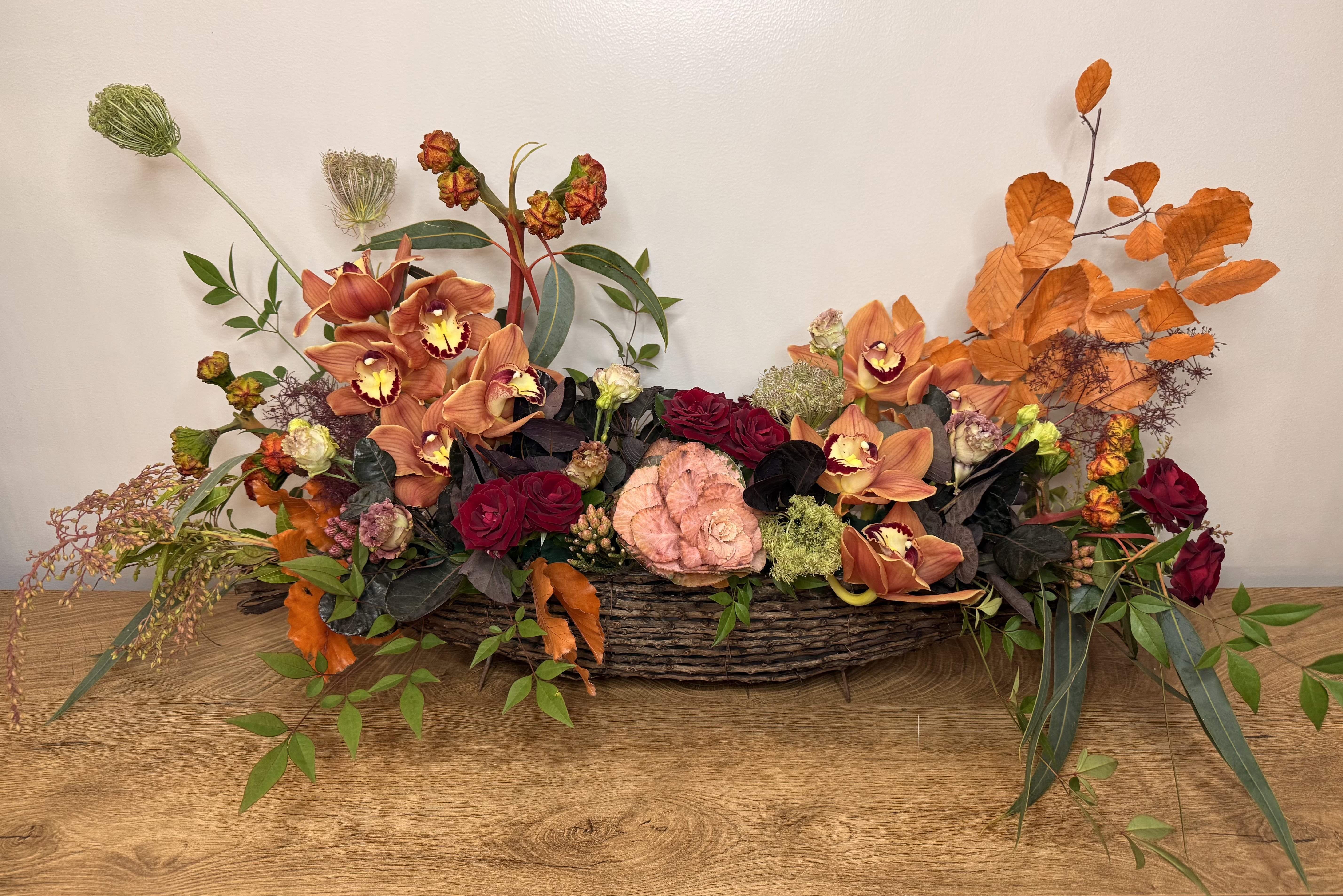 Low floral centerpiece in a woven basket with orange orchids and red roses