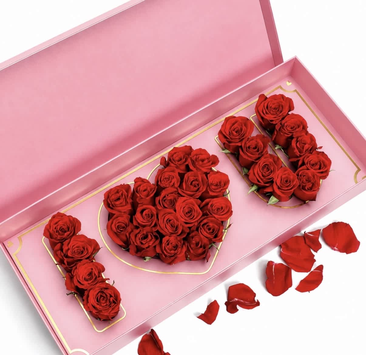 Red roses arranged in a pink gift box with scattered petals