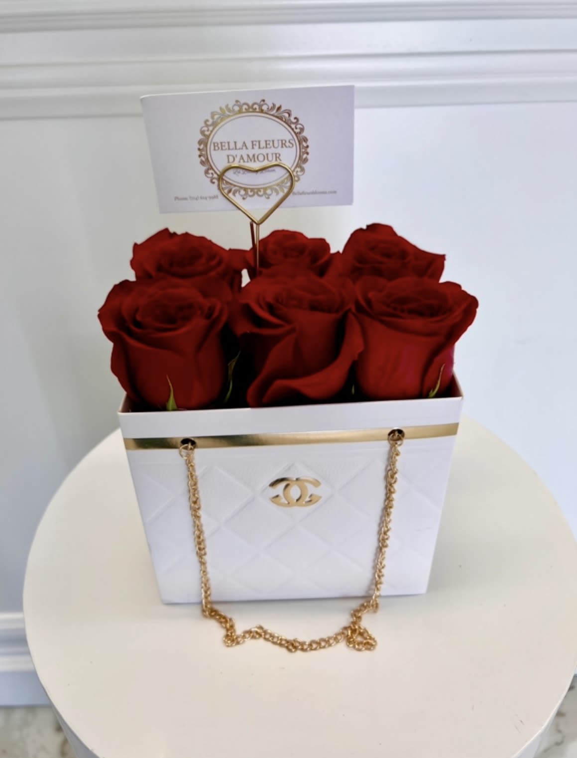 Red roses arranged in a white gift box with a gold chain handle