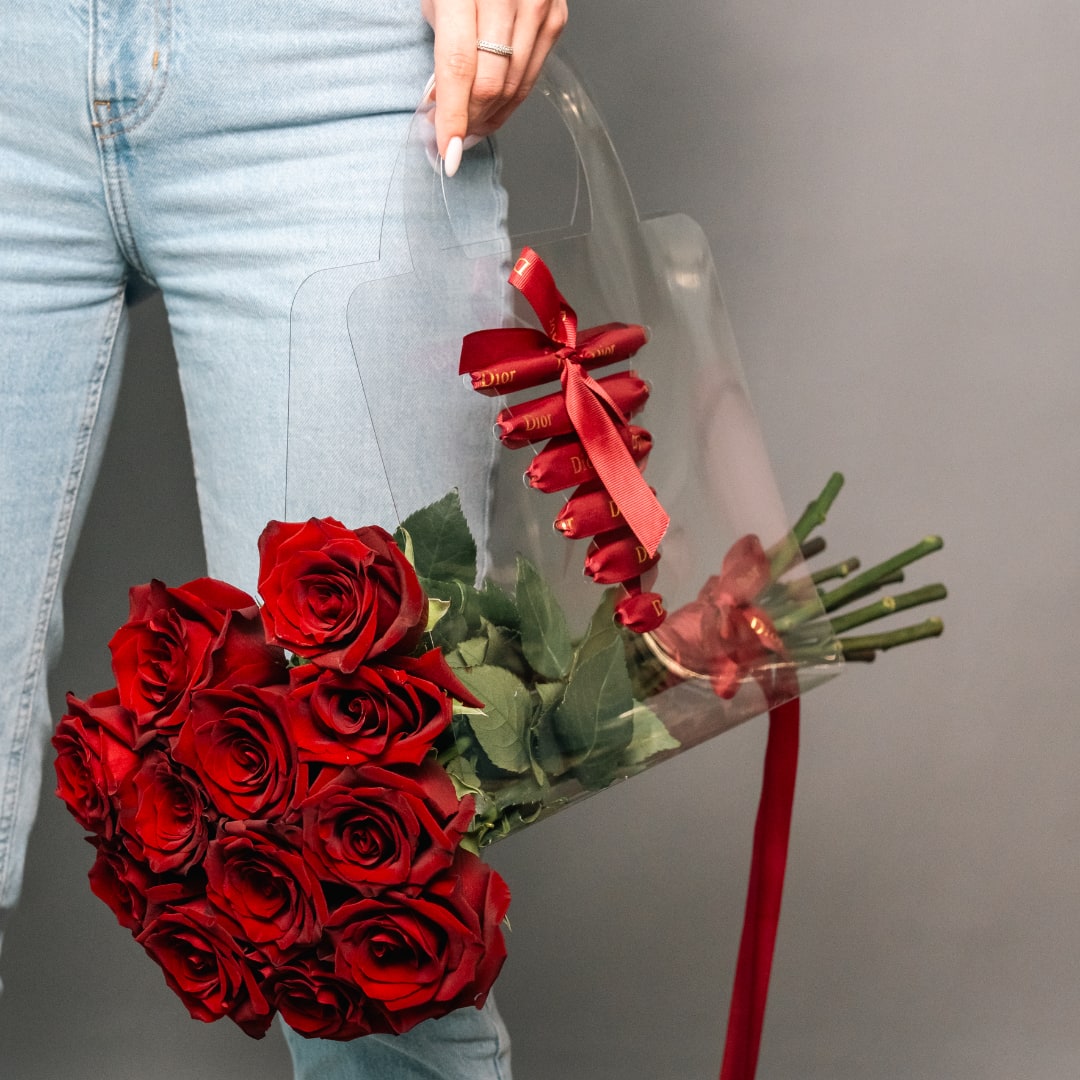 Handheld bouquet of red roses wrapped in clear plastic with a red ribbon