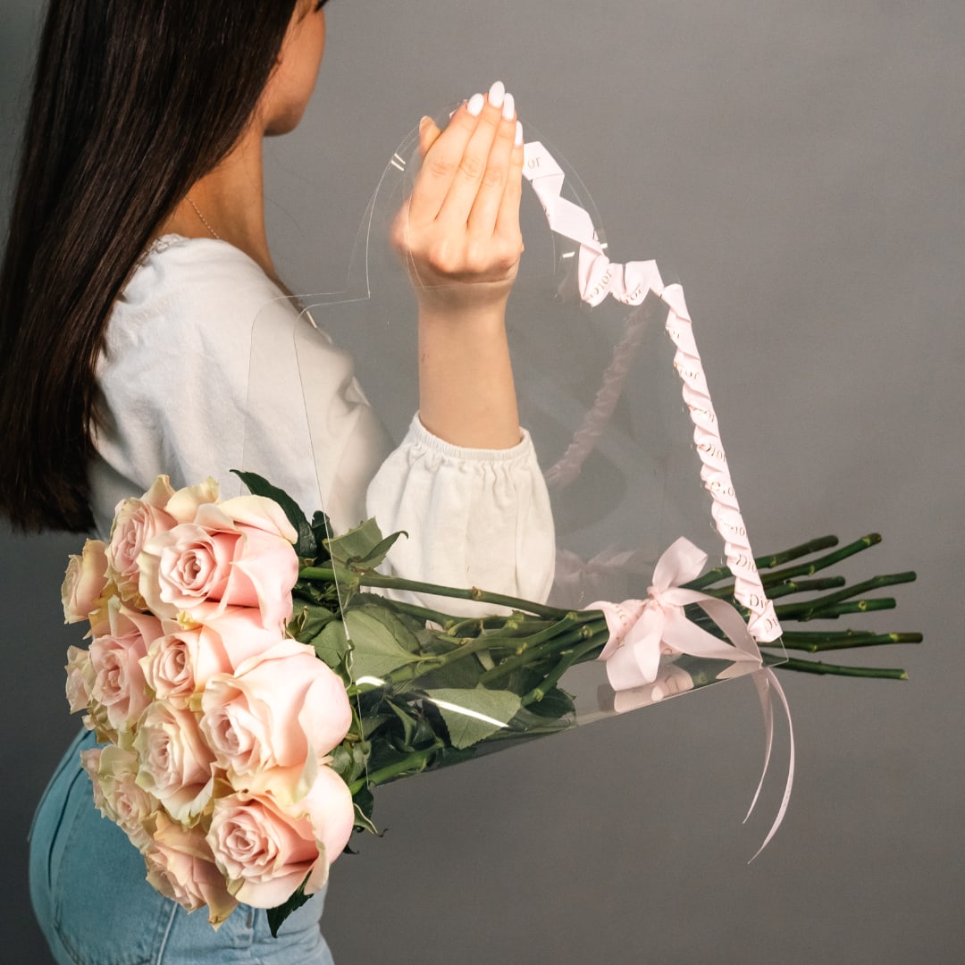 Woman holding a bouquet of pale pink roses wrapped in clear plastic
