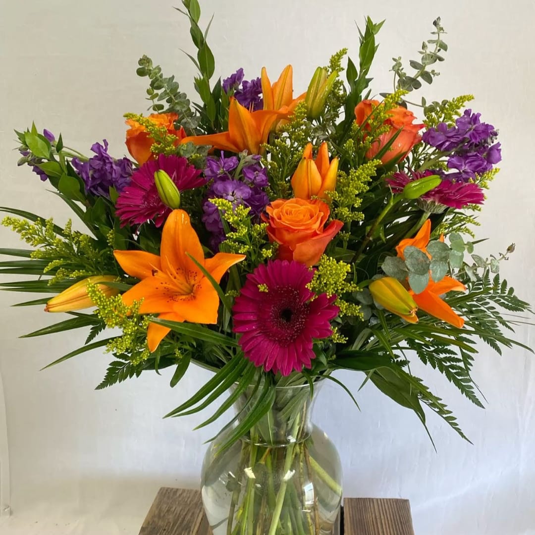Bouquet of orange lilies, roses, and purple flowers in a glass vase