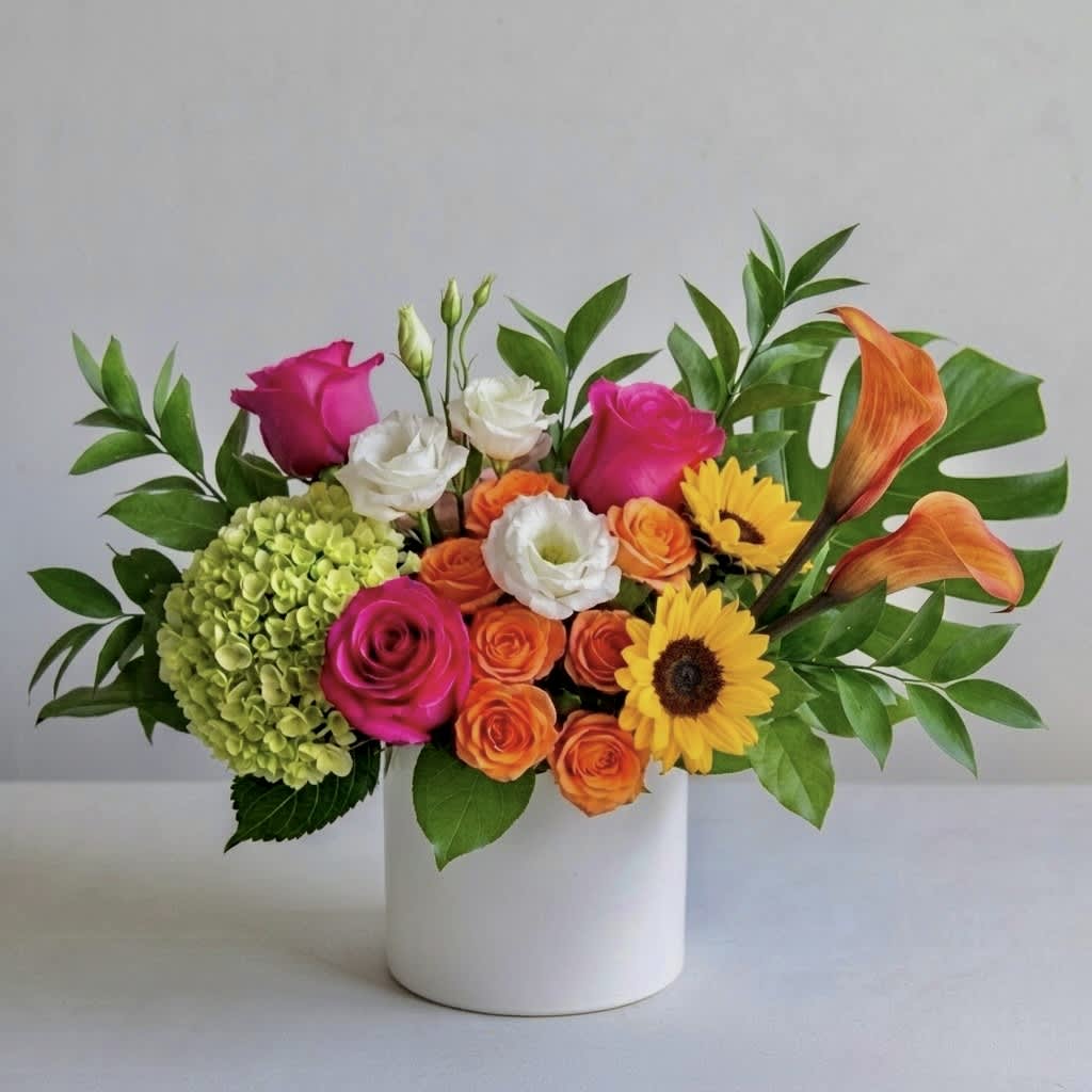 Mixed bouquet in a white vase with roses, hydrangea, calla lilies, and sunflowers