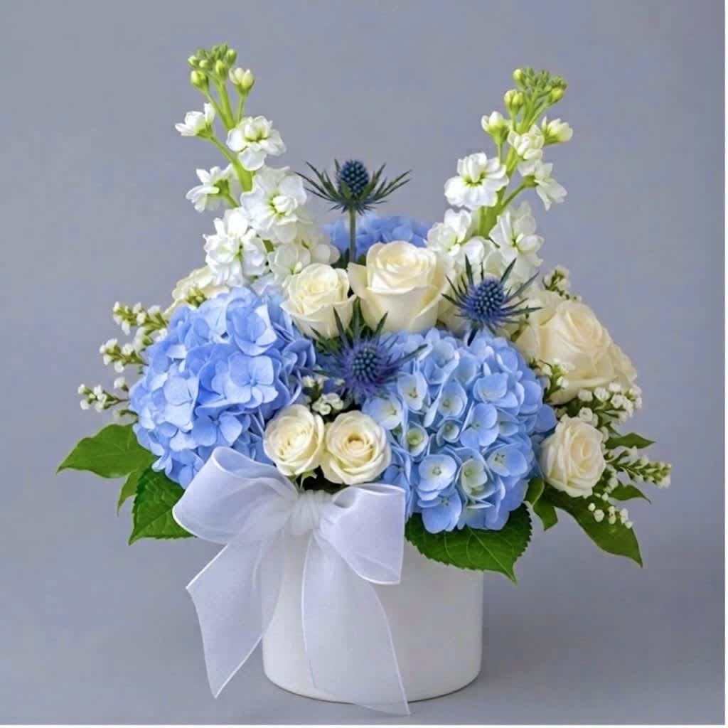 Blue hydrangeas and white roses arranged in a white box with a ribbon