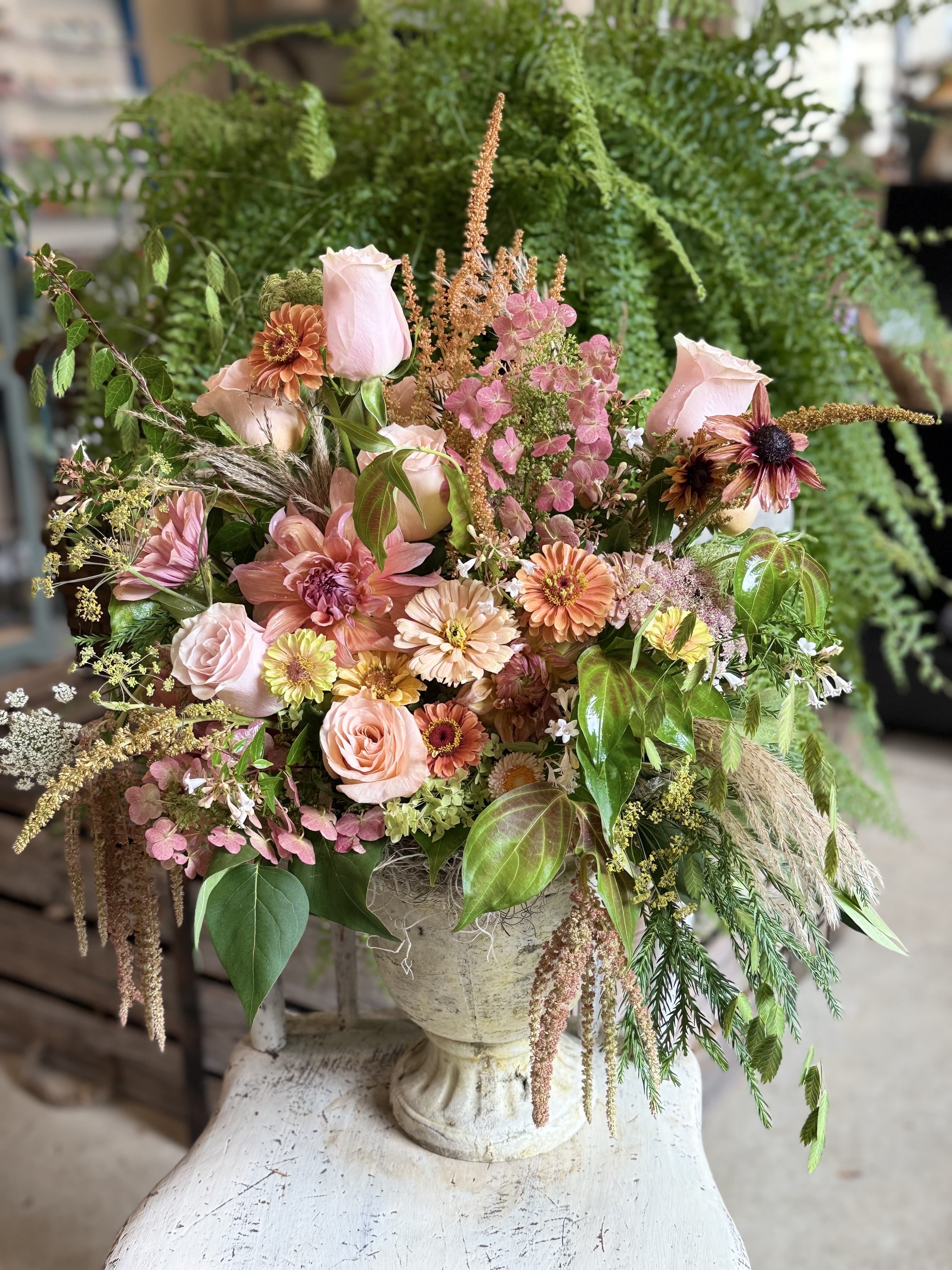 Peaches and Dreams  - Soft peach and blush roses tumble from a classical stone urn in this Peaches and Dreams flower arrangement-perfect as a birthday bouquet, anniversary gift, or a thoughtful way to say you're thinking of her. The overall impression is romantic and garden-inspired: gentle pinks, creamy whites, and warm peach tones combine to create a feminine, comforting presence that will make the recipient feel truly seen and celebrated.  This overflowing design mixes garden roses, zinnias, and clusters of small pink hydrangea, layered with airy textural accents and trailing greenery for a loose, abundant silhouette. The stone urn adds a timeless, sculpted weight that suits mantelpieces, dining tables, or an entryway; the palette reads soft and luminous rather than formal, so it fits both everyday display and special occasions.  Send this arrangement to mark a milestone, brighten someone's recovery, or bring a soft touch to a table centerpiece-the kind of gift that comforts and delights. Sizes are built around the urn style shown; please note delicate blooms benefit from fresh water and a cool spot away from direct sun to prolong their life.