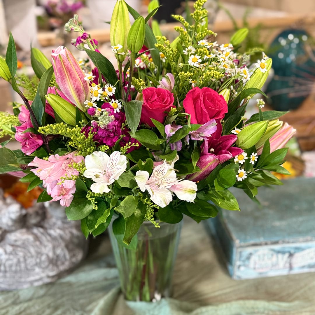Mixed bouquet of pink roses, lilies, and small white daisies in a glass vase
