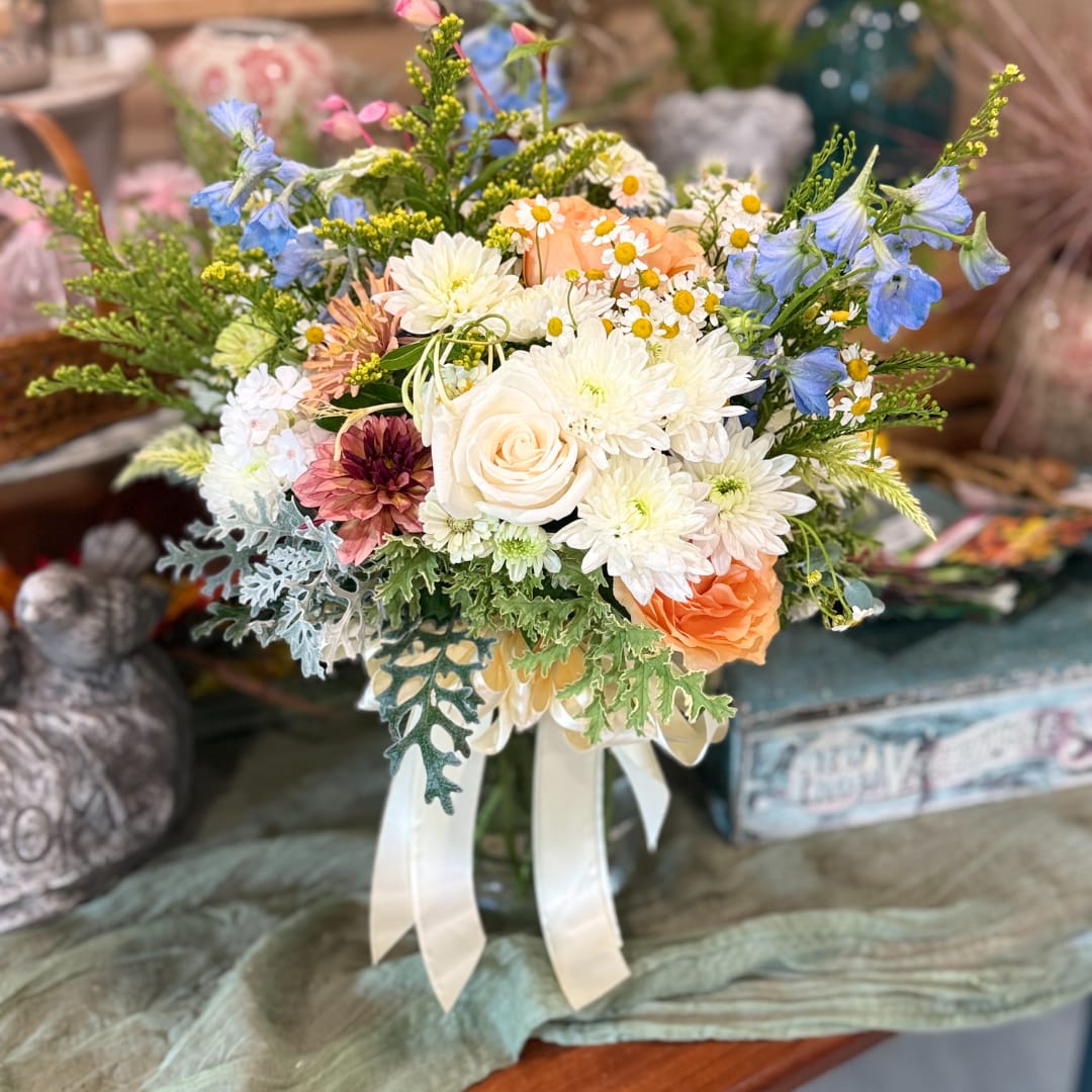 Bouquet of white, peach, and blue flowers tied with white ribbon