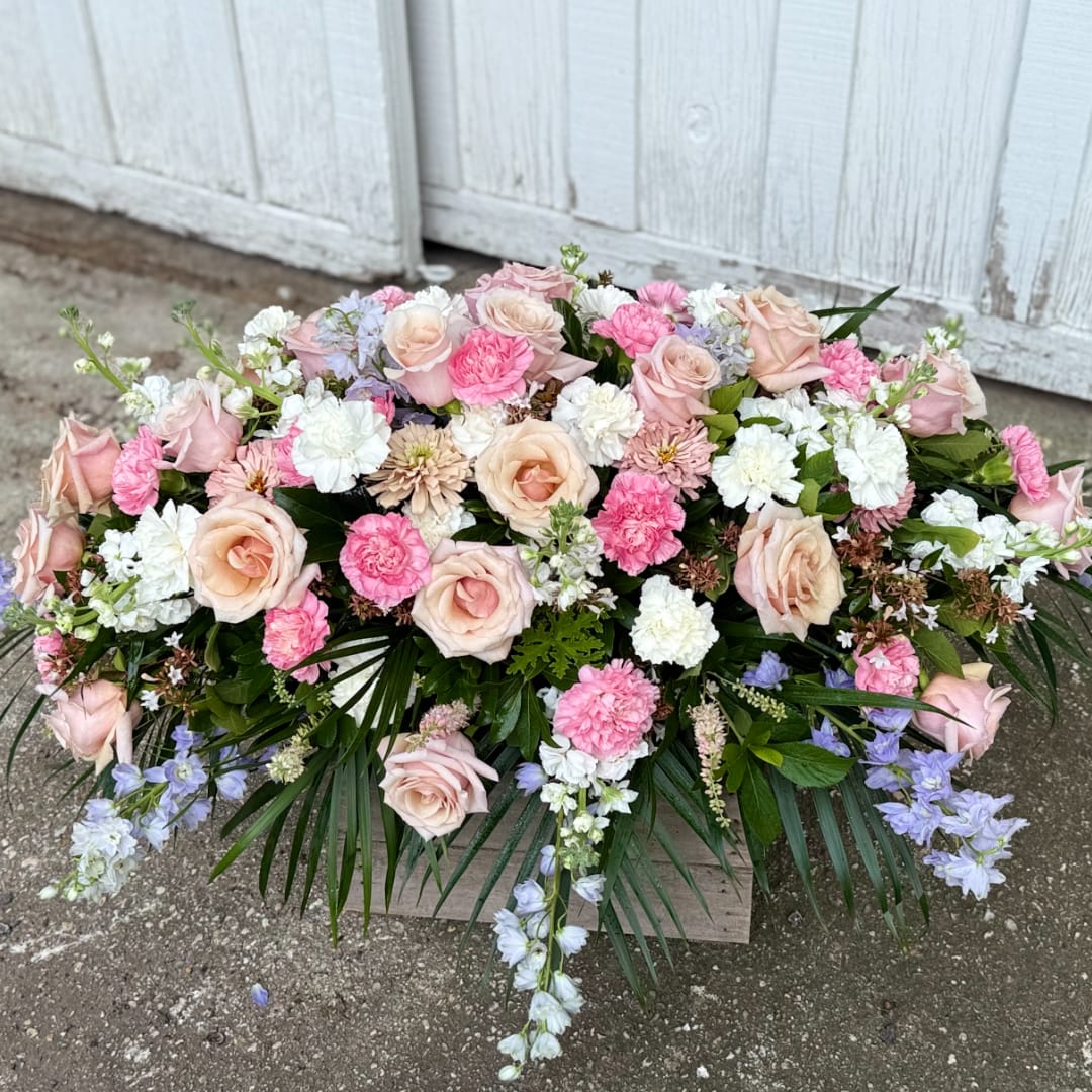 Large pastel floral arrangement with roses, carnations, and blue flowers in a wooden box