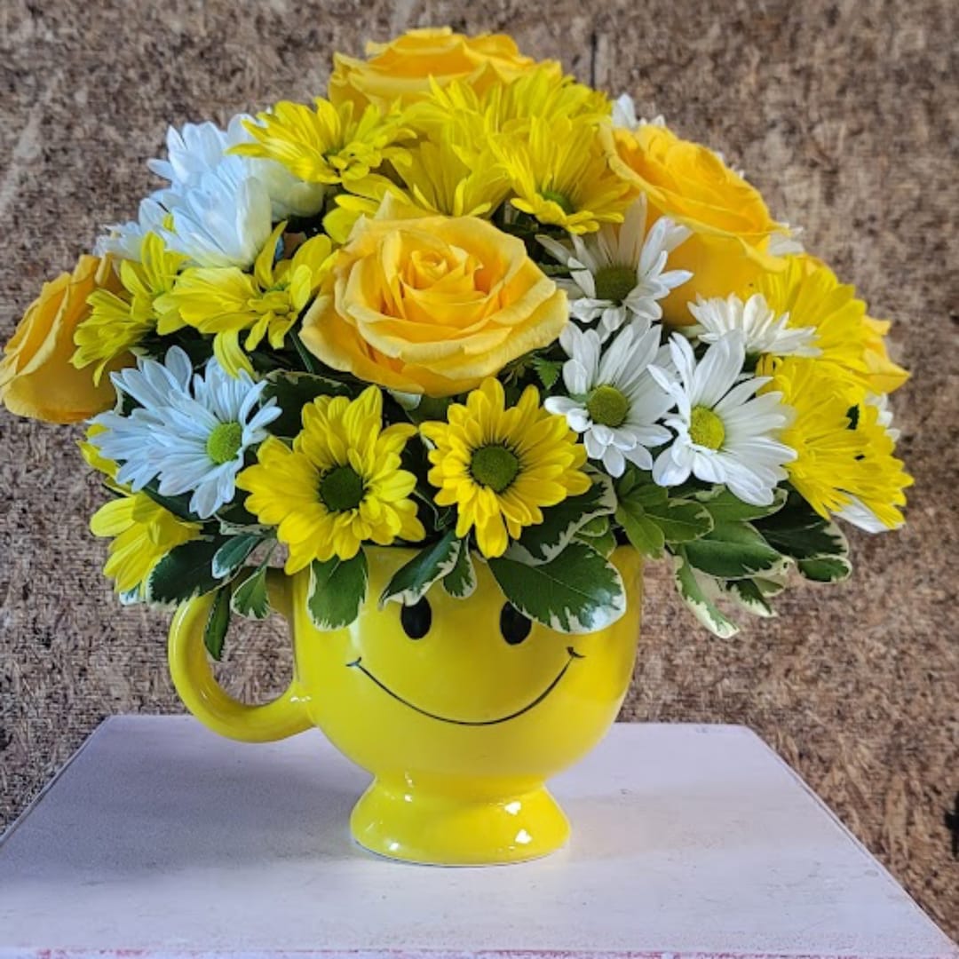 Yellow and white flower arrangement in a smiley-face mug
