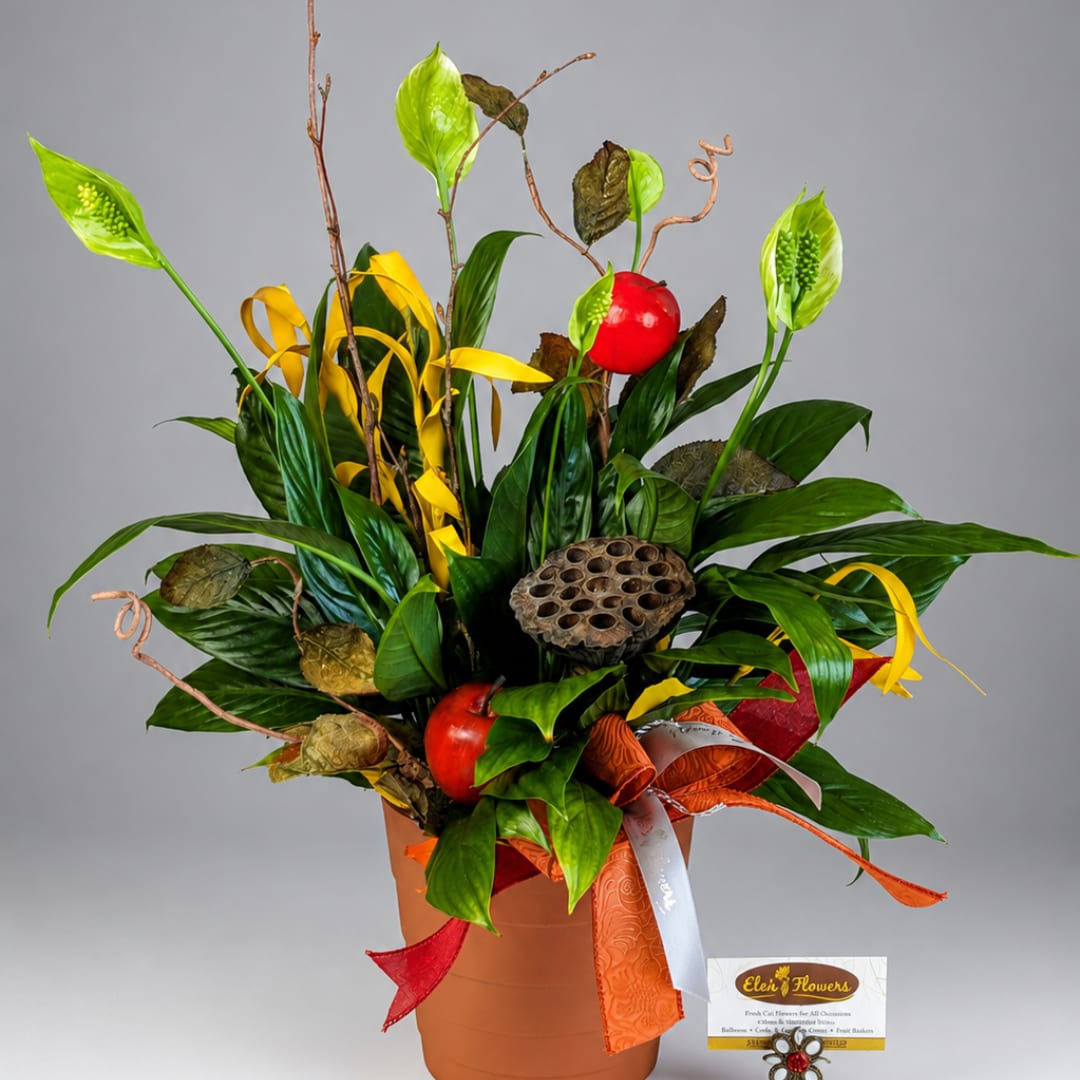 Tropical arrangement with green leaves, red accents, and ribbon in a terracotta pot