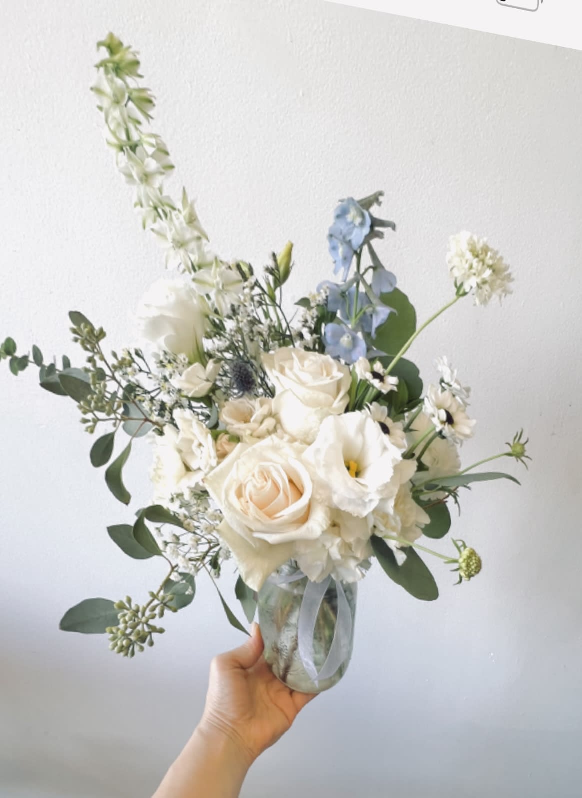 White and pale blue bouquet in a glass jar vase