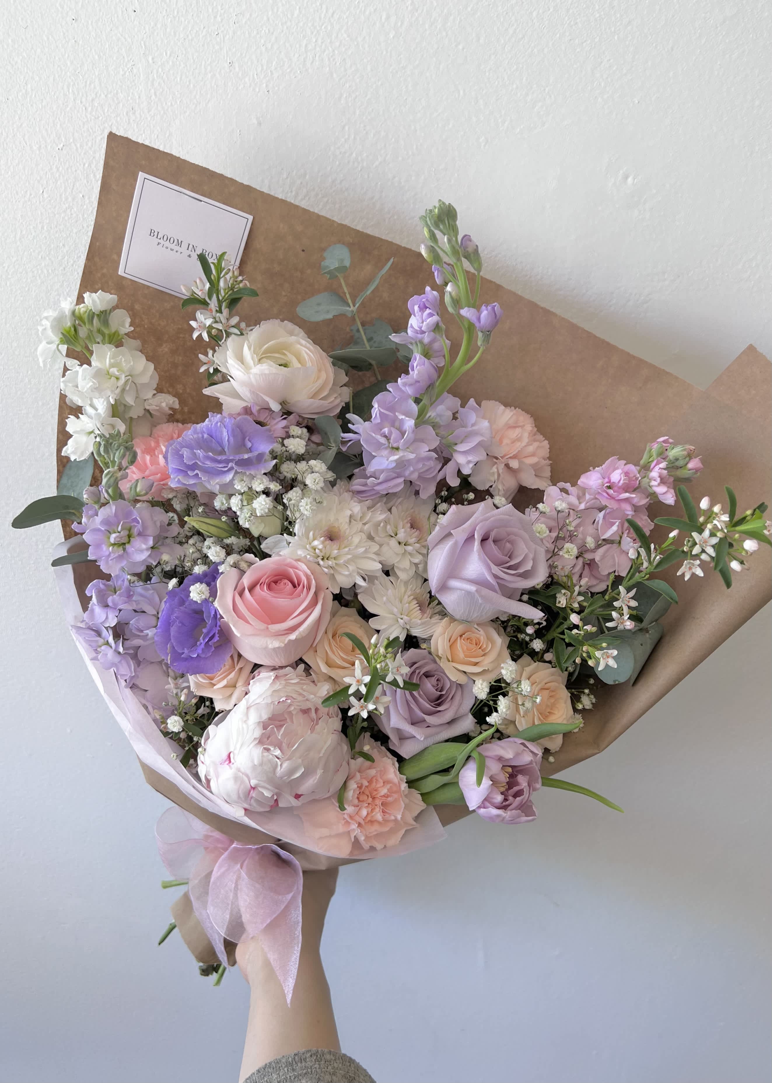 Pastel bouquet of roses, peonies, and lavender flowers wrapped in brown paper