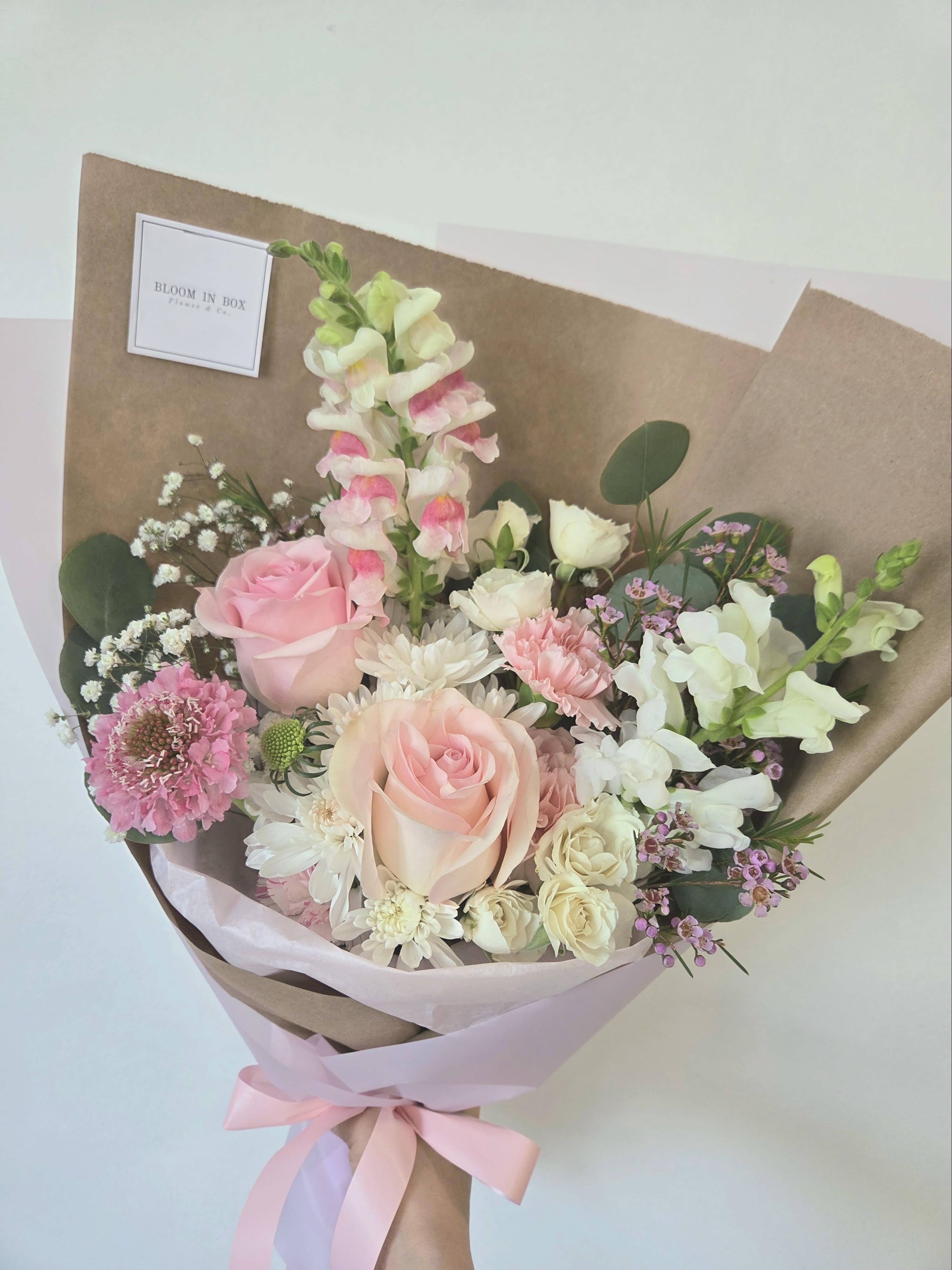 Hand-tied bouquet of pink and white flowers wrapped in brown paper