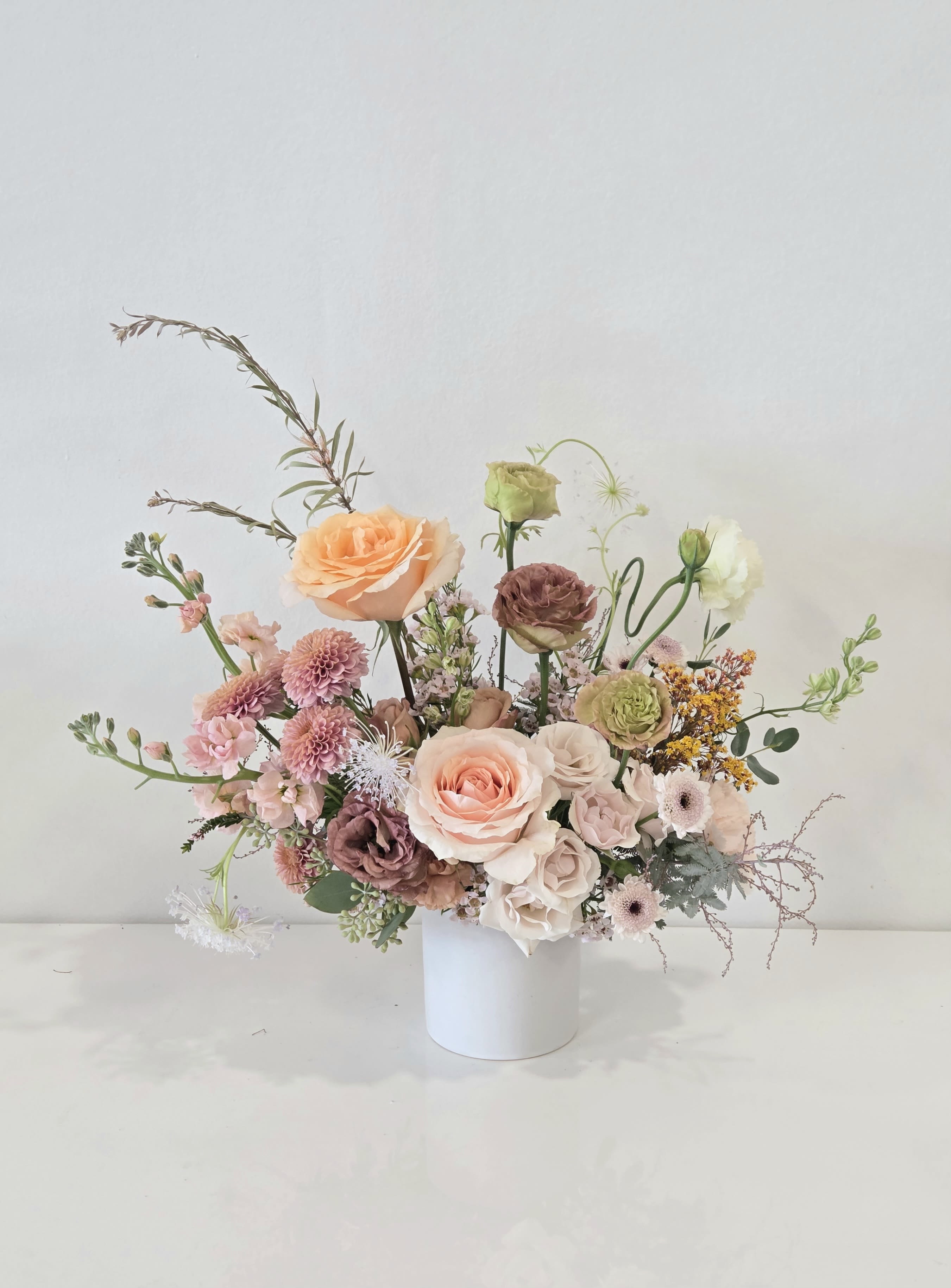 Asymmetrical arrangement of peach and blush flowers in a white cylinder vase