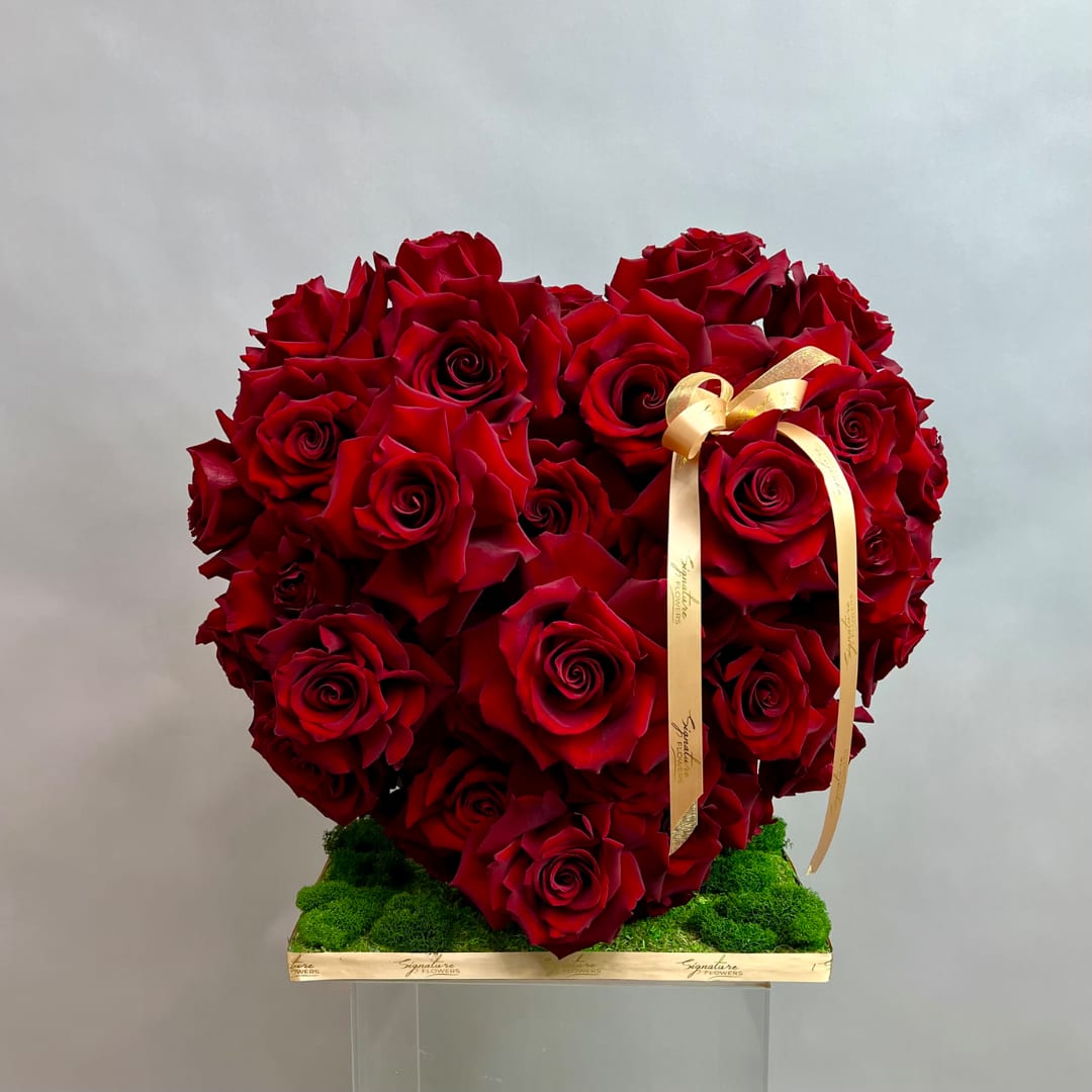 Heart-shaped arrangement of red roses with a gold ribbon on a green base