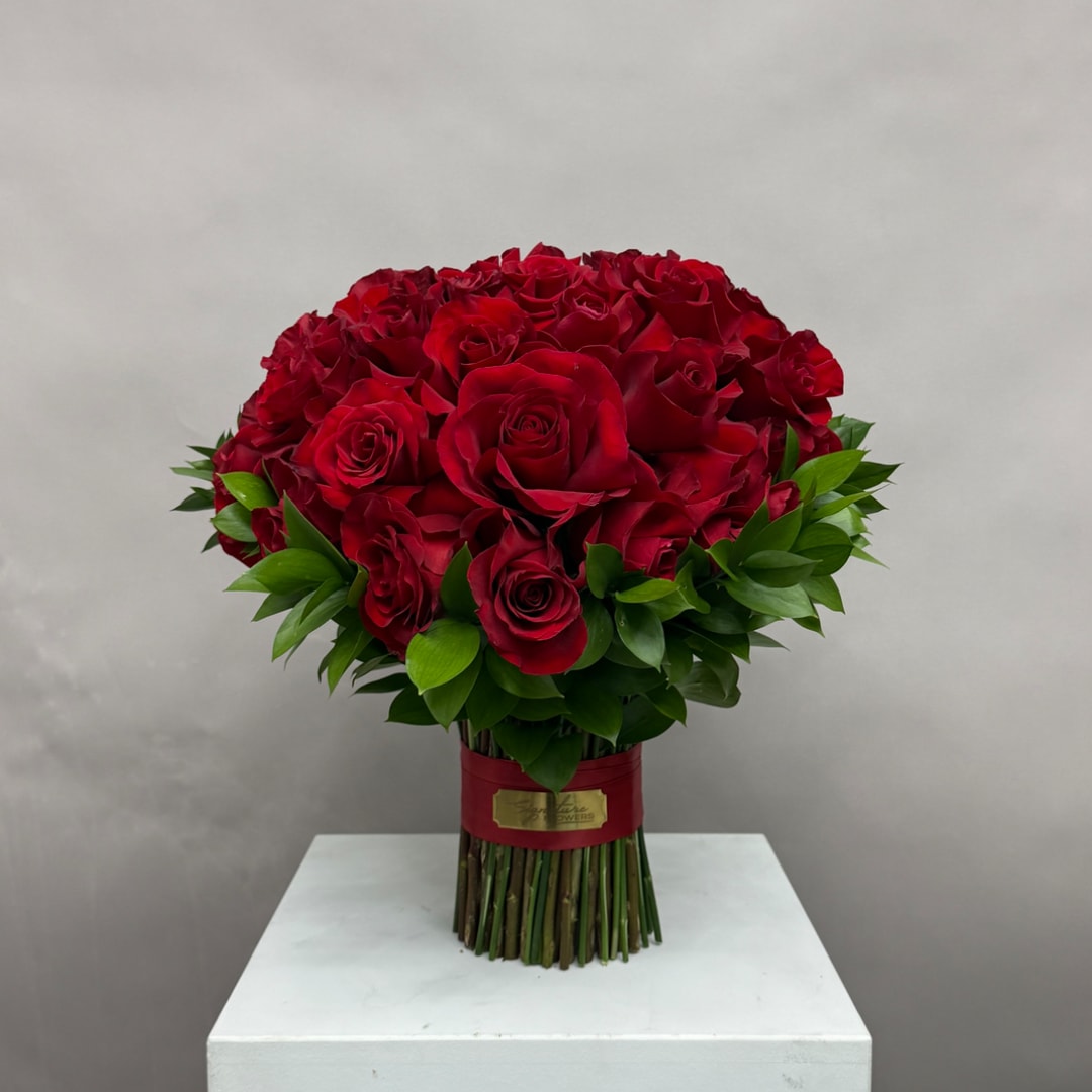 Bouquet of red roses with green foliage tied at the stems