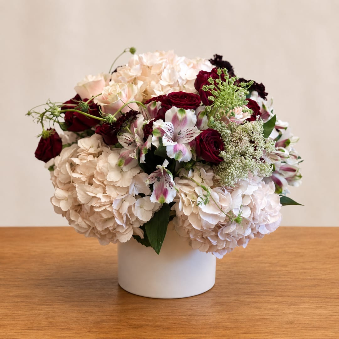 Bouquet of cream hydrangeas, red roses, and white alstroemeria in a white vase