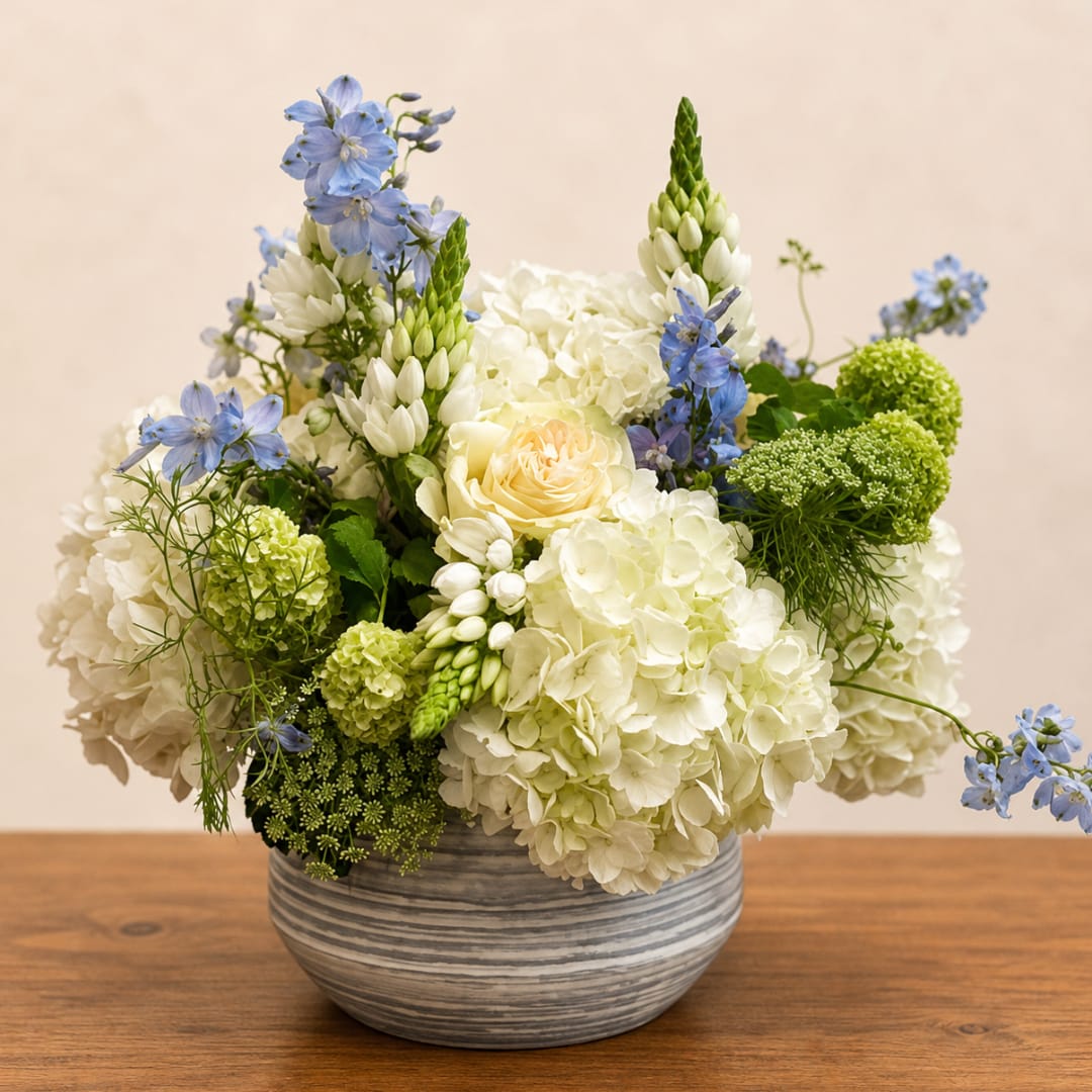 White hydrangea and blue flower arrangement in a striped ceramic bowl