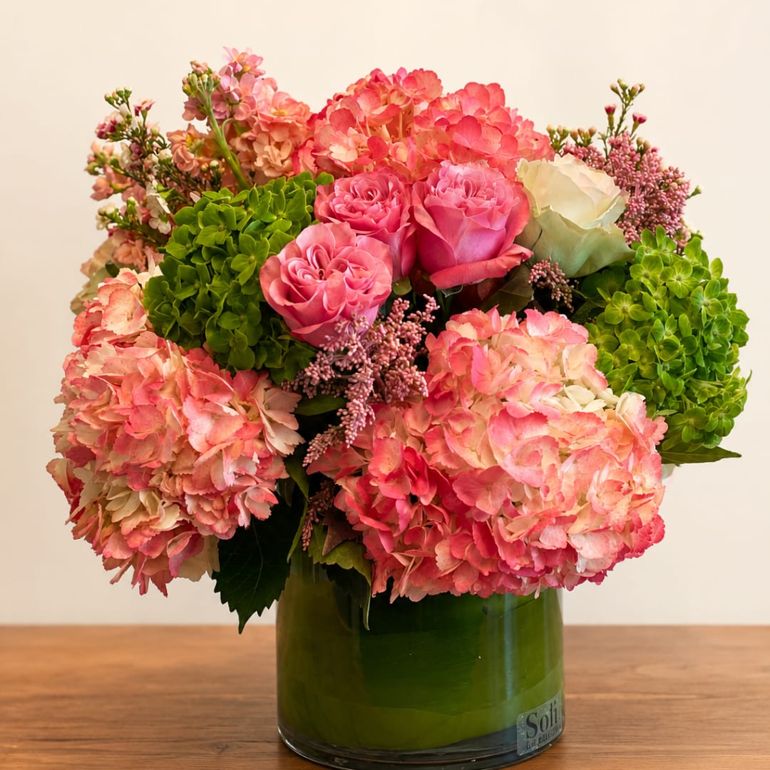 Pink hydrangeas and roses arranged in a green glass vase