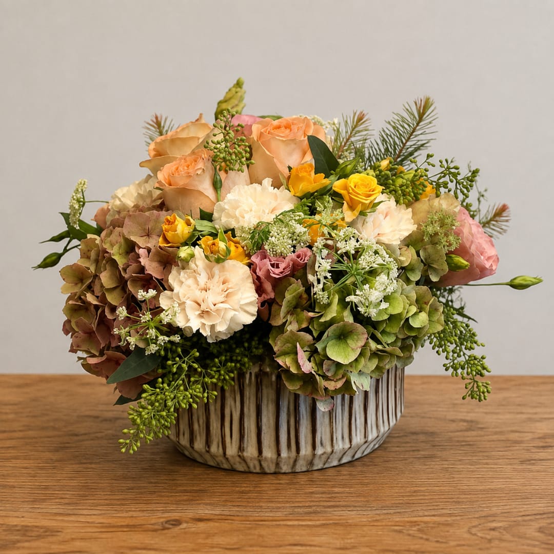 Mixed bouquet of peach roses, hydrangeas, and yellow spray roses in a ceramic vase