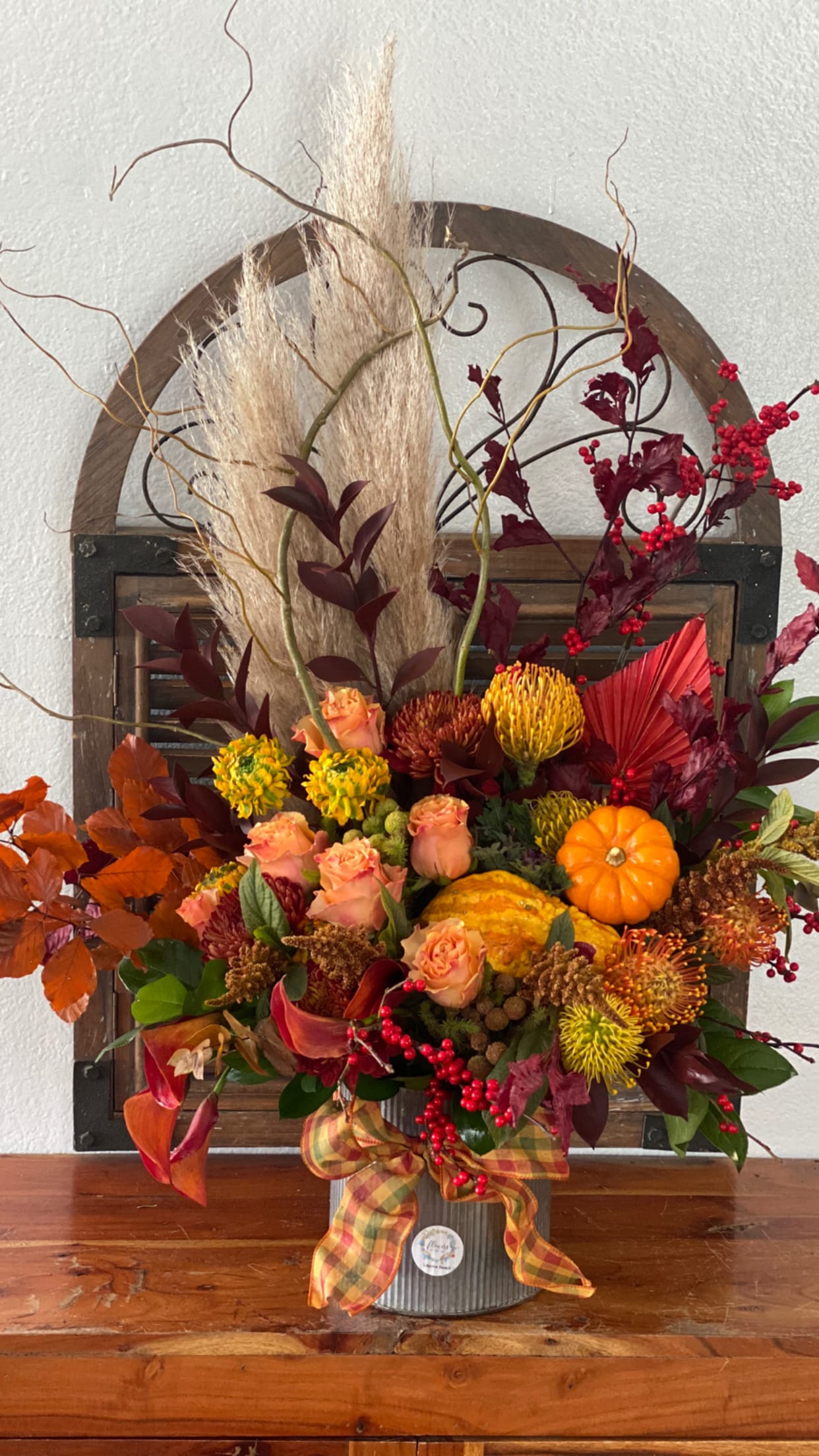 Autumn floral arrangement with roses, mums, and pumpkins in a metal container